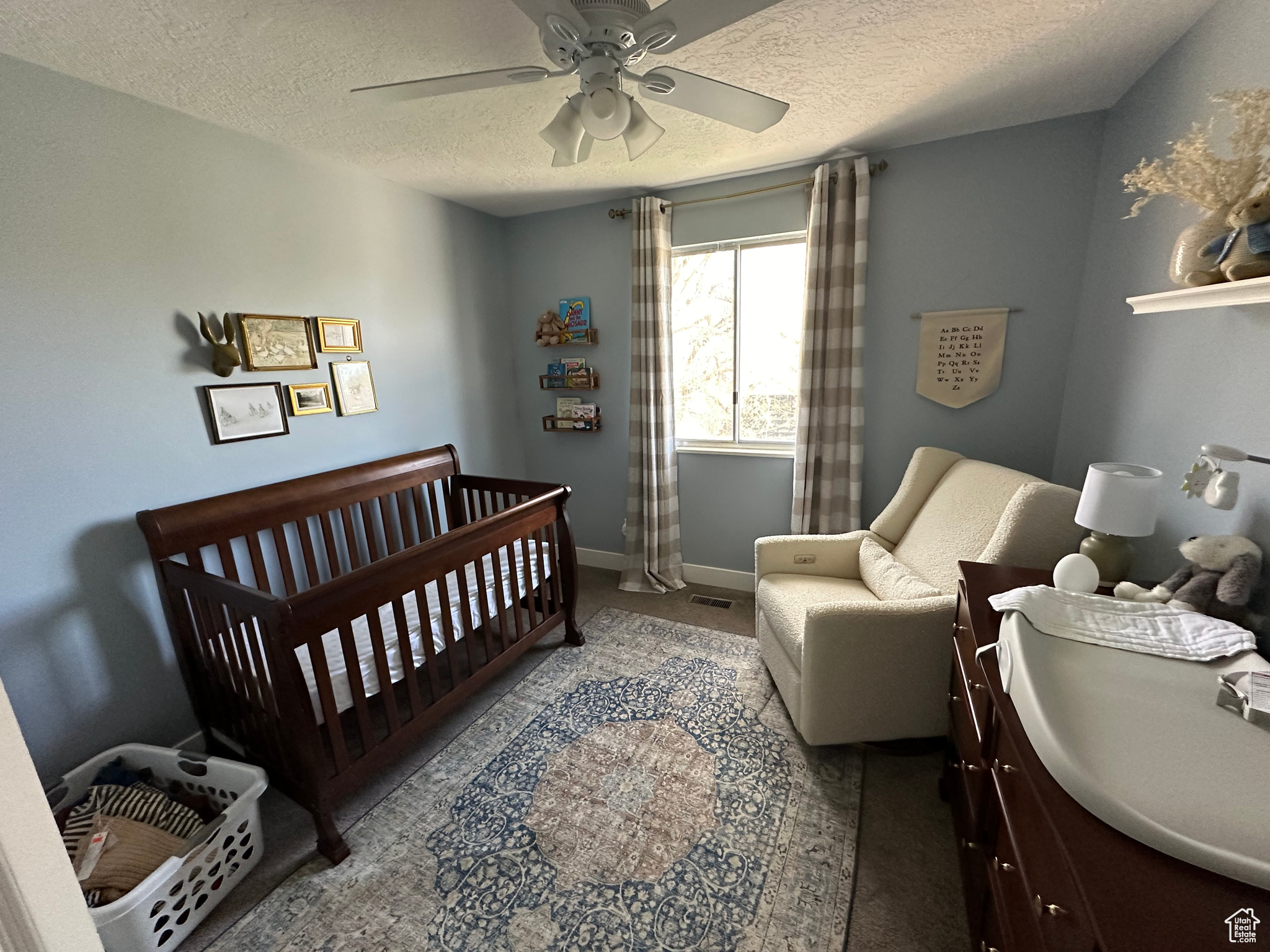 Bedroom with a textured ceiling, carpet floors, ceiling fan, and a nursery area