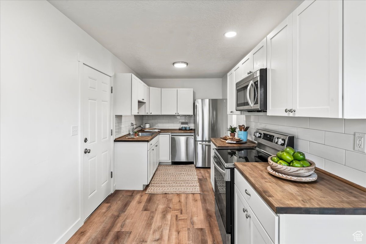 Kitchen featuring backsplash, hardwood / wood-style floors, wood counters, and stainless steel appliances