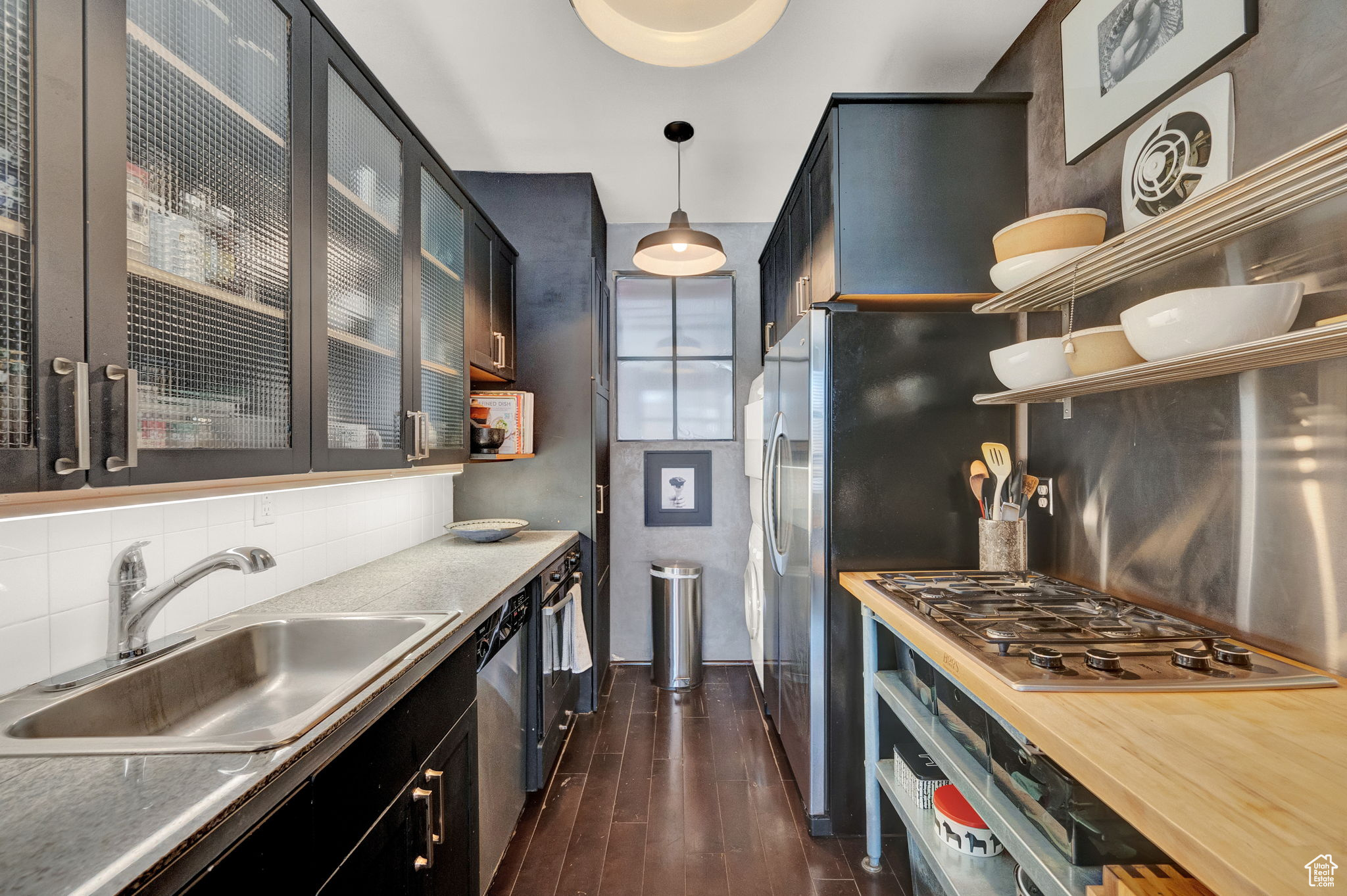 Kitchen with hanging light fixtures, backsplash, stainless steel appliances, dark wood-type flooring, and sink