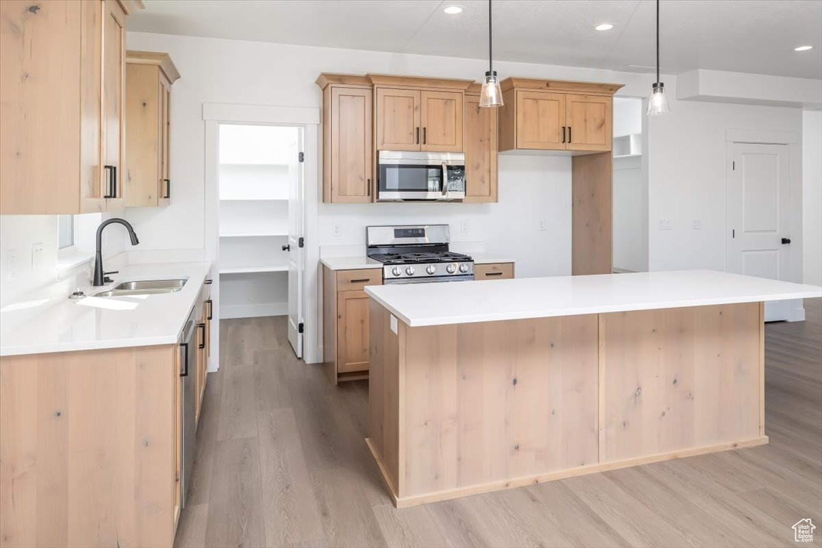 Kitchen featuring a center island, light brown cabinetry, light hardwood / wood-style floors, decorative light fixtures, and stainless steel appliances