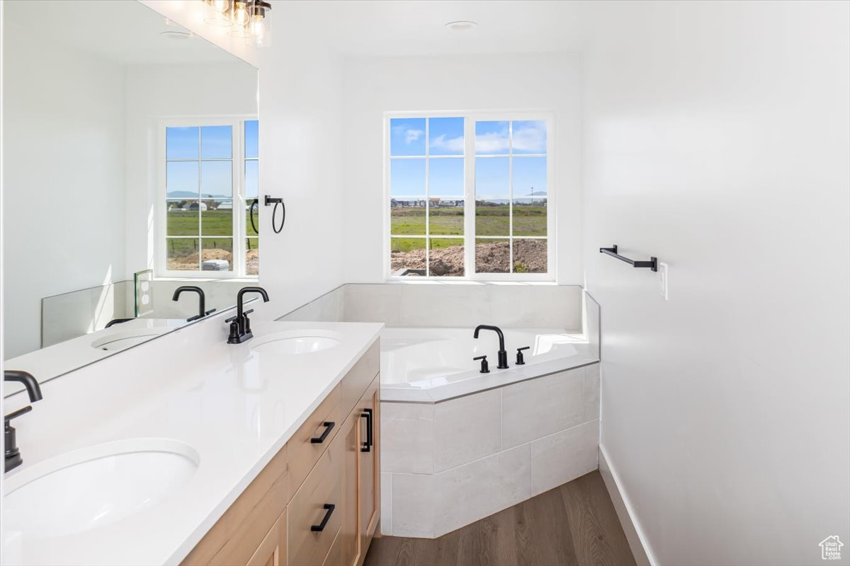 Bathroom featuring a relaxing tiled bath, hardwood / wood-style flooring, and double sink vanity