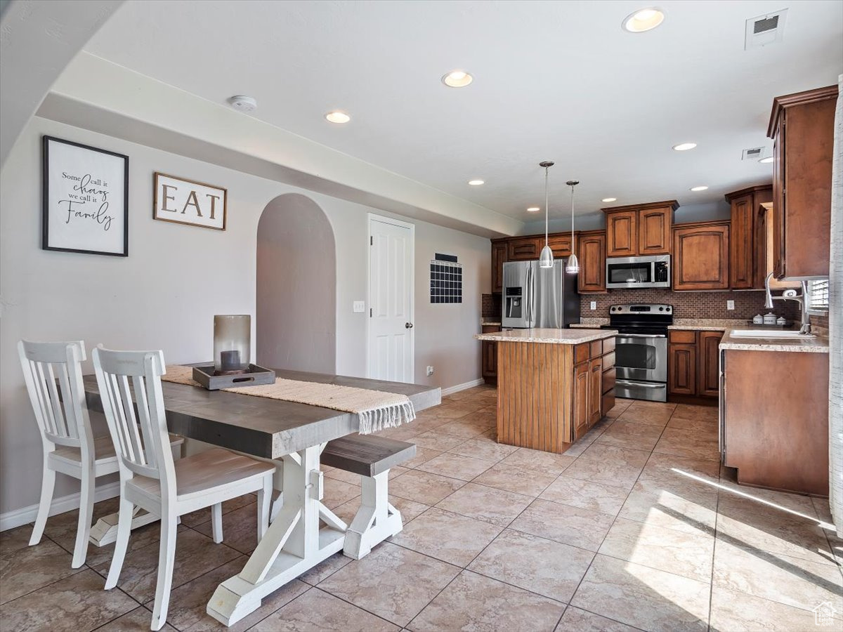 Kitchen with stainless steel appliances, a kitchen island, sink, backsplash, and tile flooring