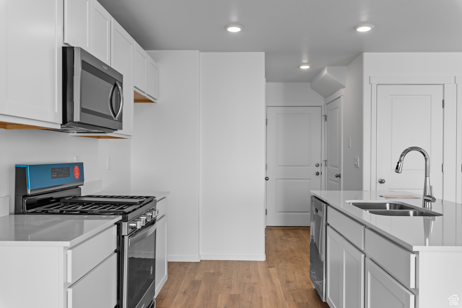 Kitchen with white cabinets, sink, stainless steel appliances, and light wood-type flooring