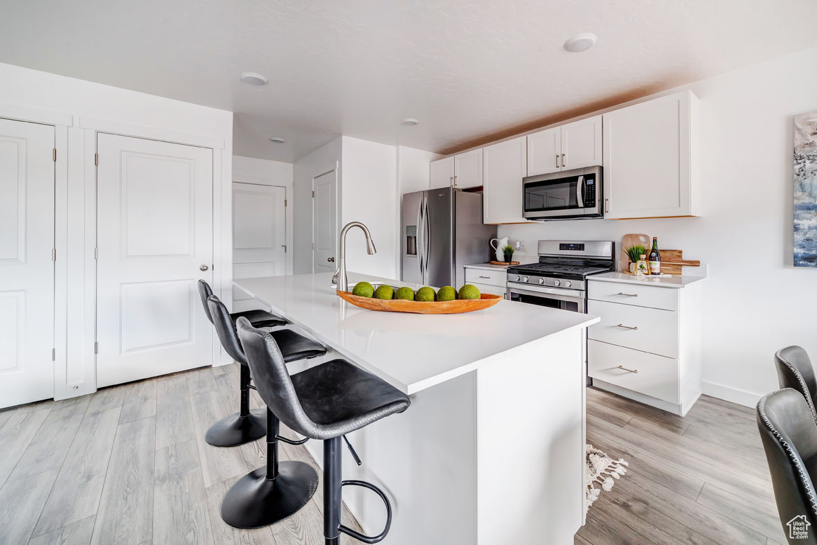 Kitchen featuring a breakfast bar, light hardwood / wood-style floors, white cabinetry, stainless steel appliances, and an island with sink