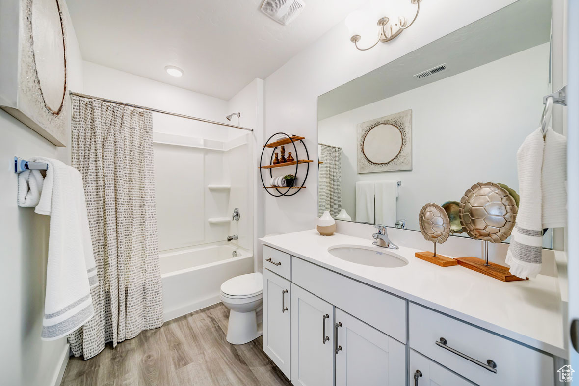 Full bathroom with hardwood / wood-style floors, vanity, toilet, and shower / bathtub combination with curtain