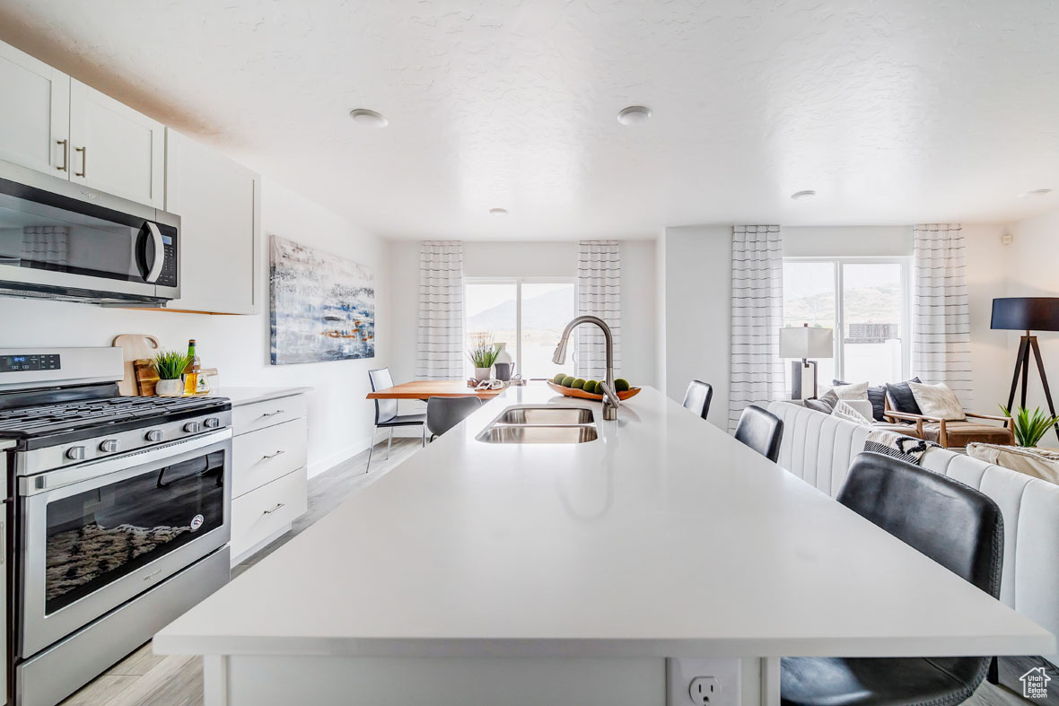 Kitchen featuring a breakfast bar, white cabinetry, appliances with stainless steel finishes, sink, and an island with sink