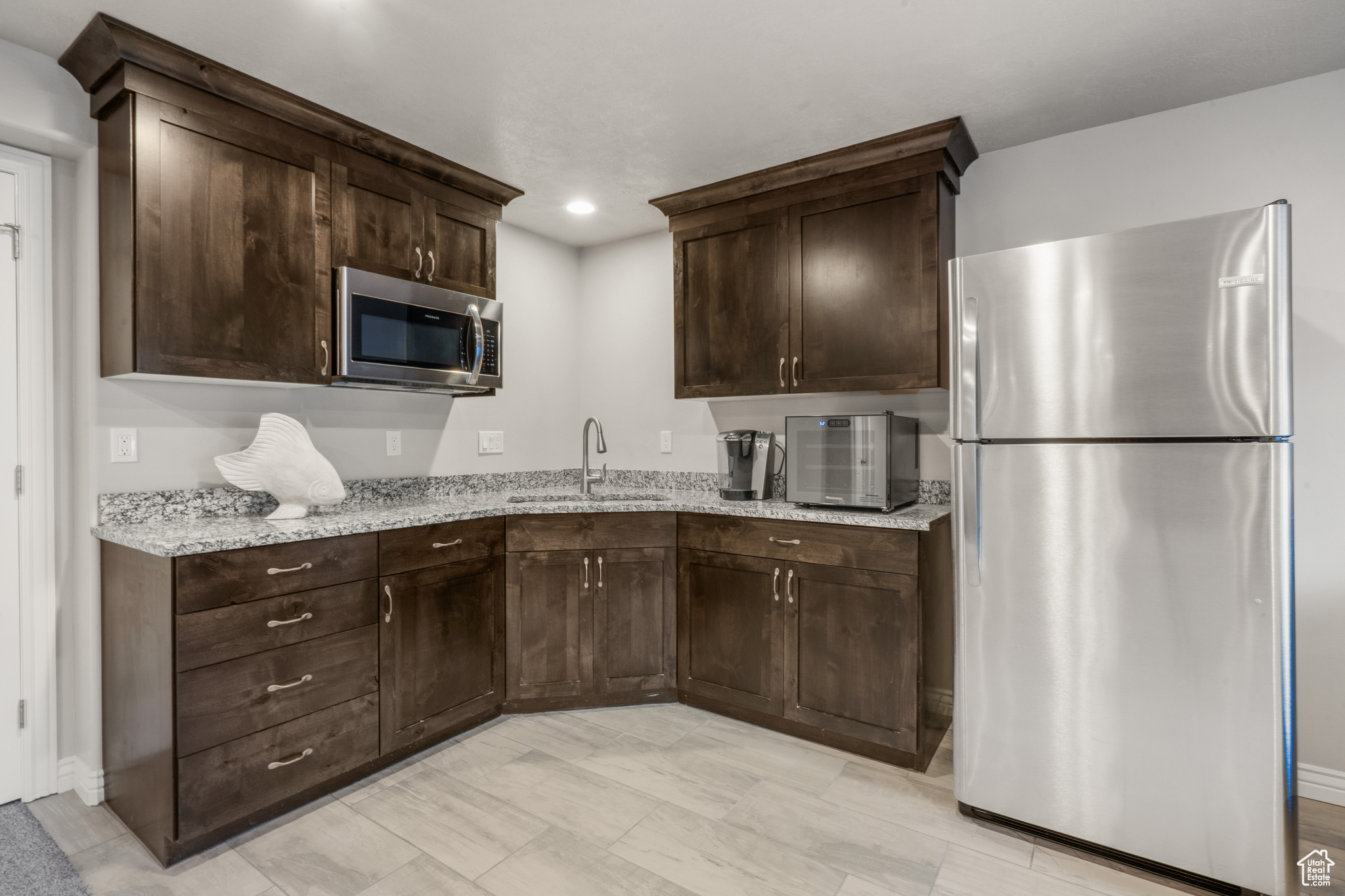 Kitchen featuring dark brown cabinetry, appliances with stainless steel finishes, light tile floors, sink, and light stone countertops