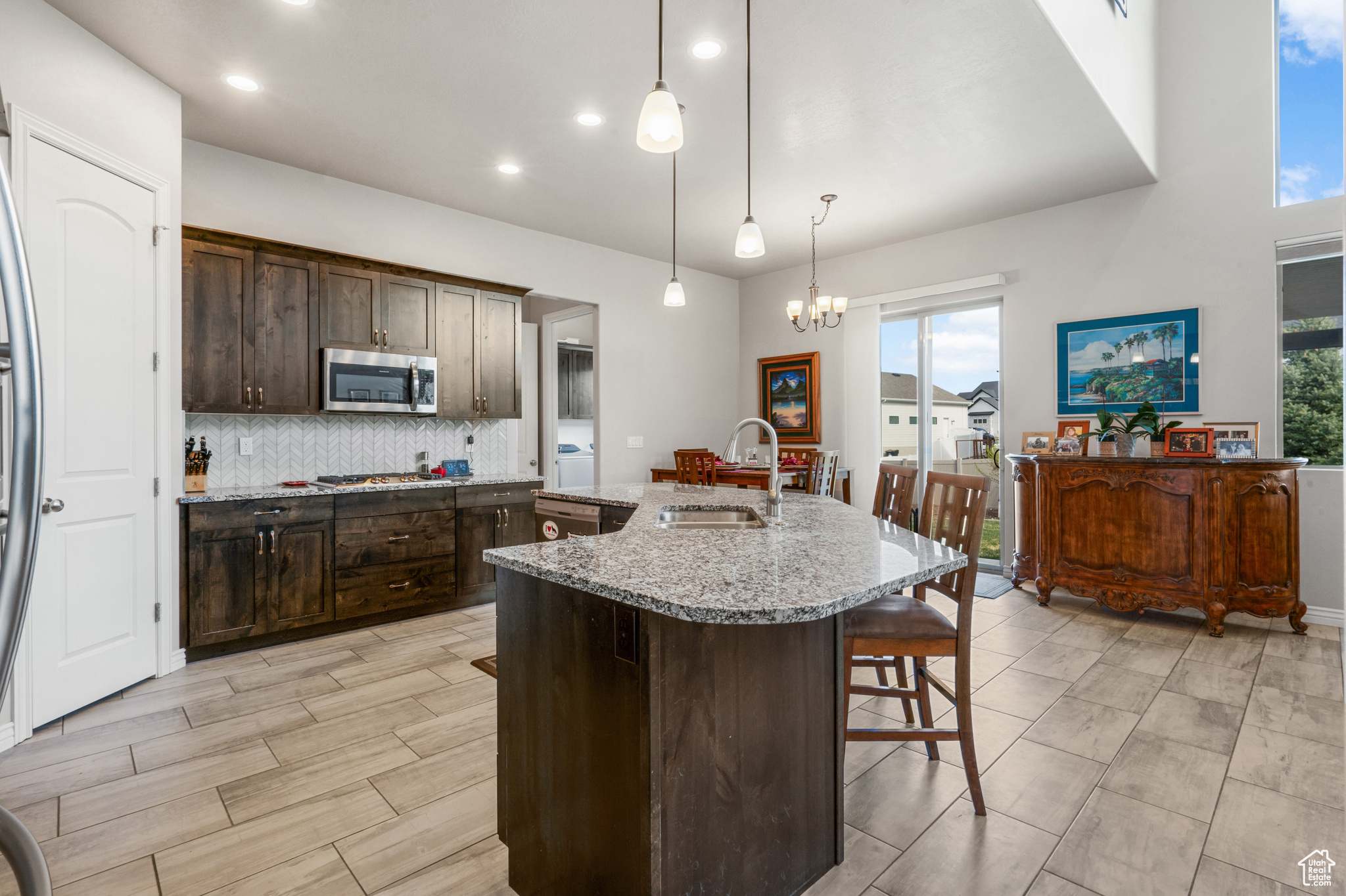 Kitchen with pendant lighting, light stone countertops, sink, tasteful backsplash, and an island with sink