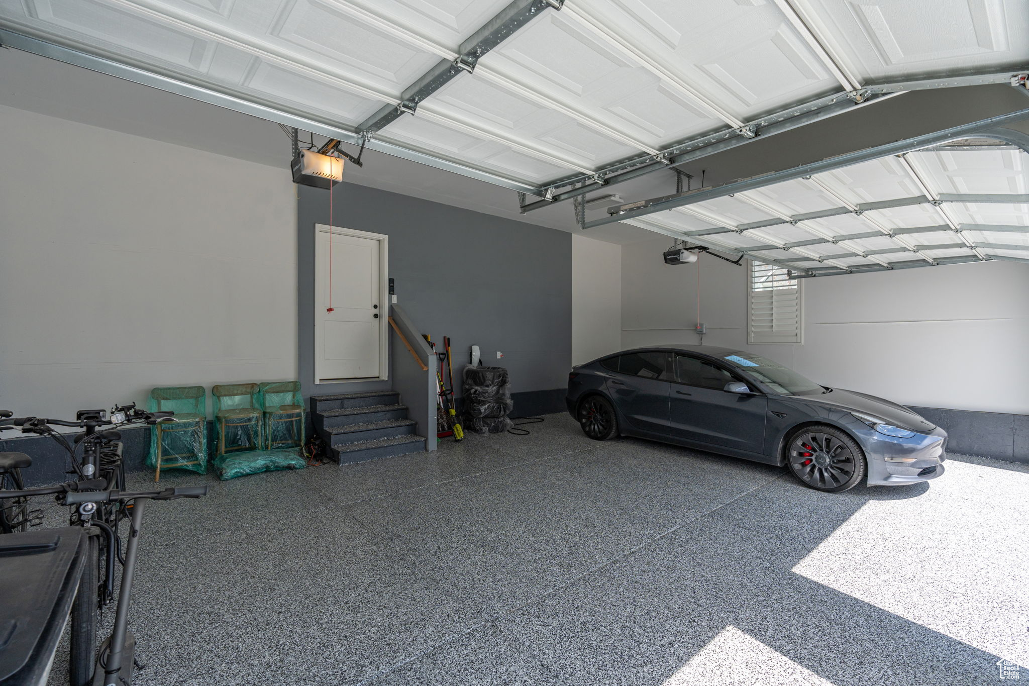 Three-car garage with finished walls, a side entry door, plantation shutters, epoxy flooring, and wiring to charge electric cars.