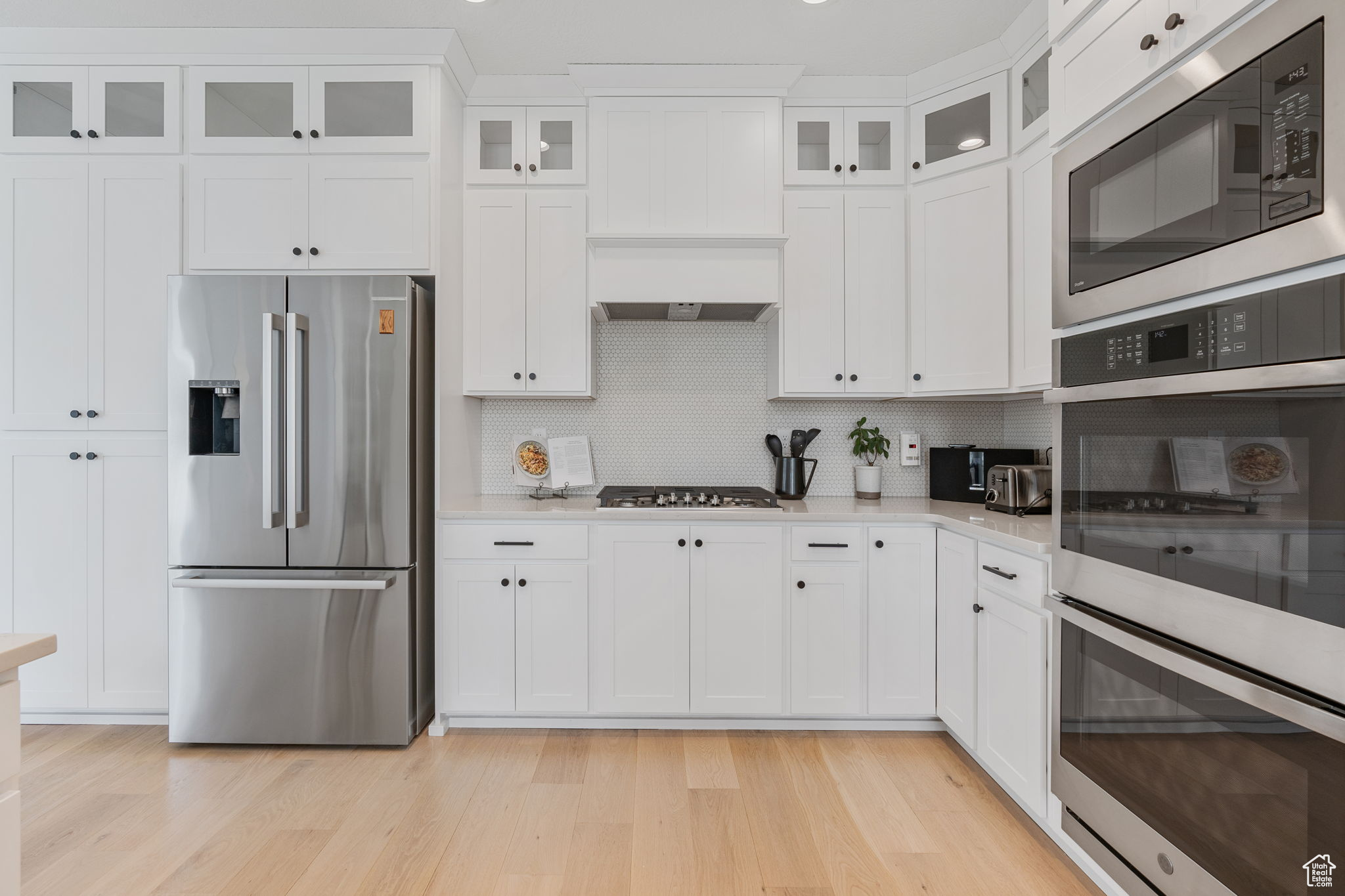 Kitchen featuring white cabinets, tasteful backsplash, white oak hardwood flooring, and stainless steel appliances.