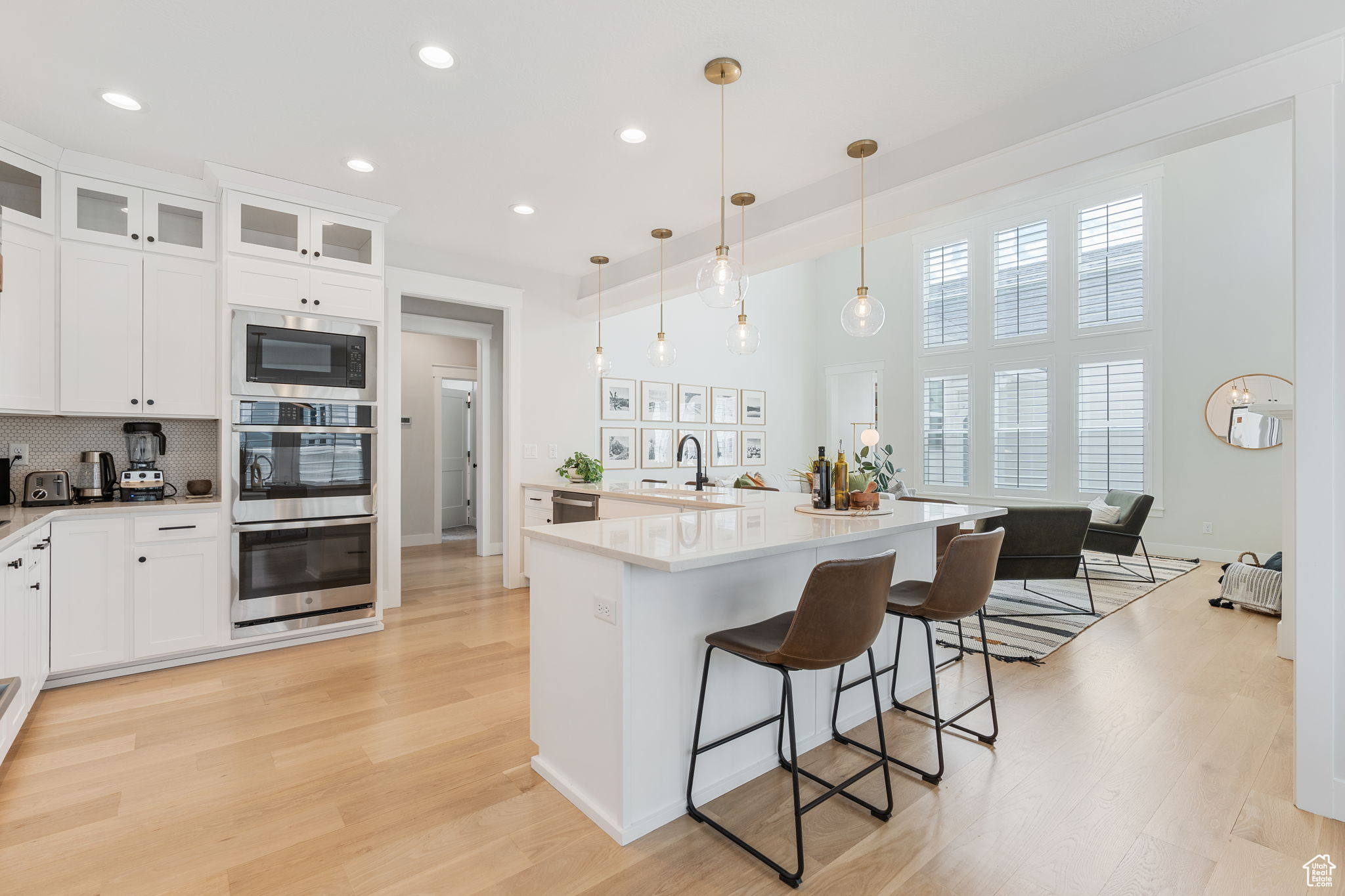 Gourmet kitchen with stainless steel appliances, white cabinetry, white oak hardwood flooring, and contemporary light fixtures.
