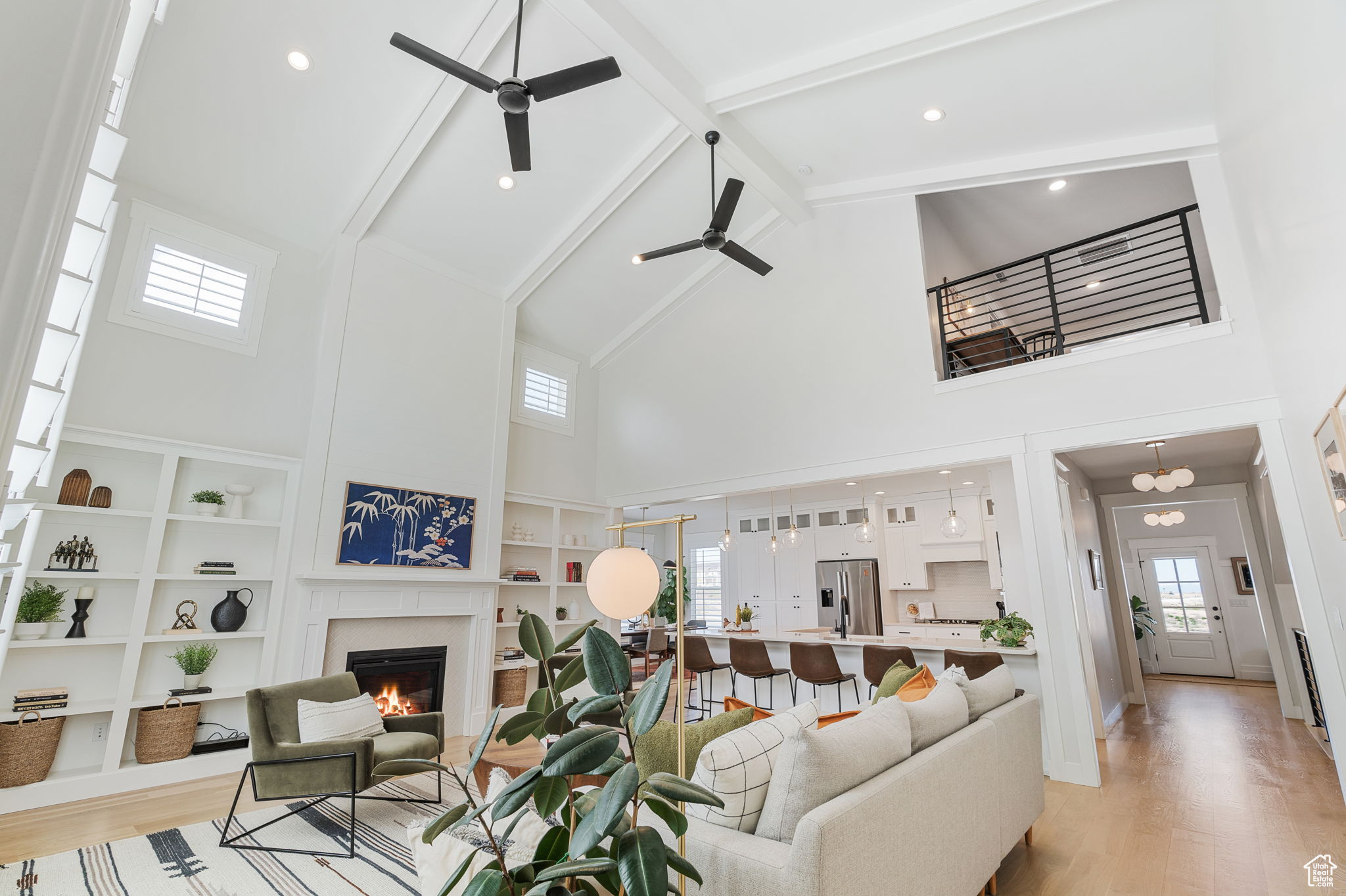 Living room with ceiling fans, built ins, high vaulted ceiling, white oak hardwood flooring, and beam ceiling.