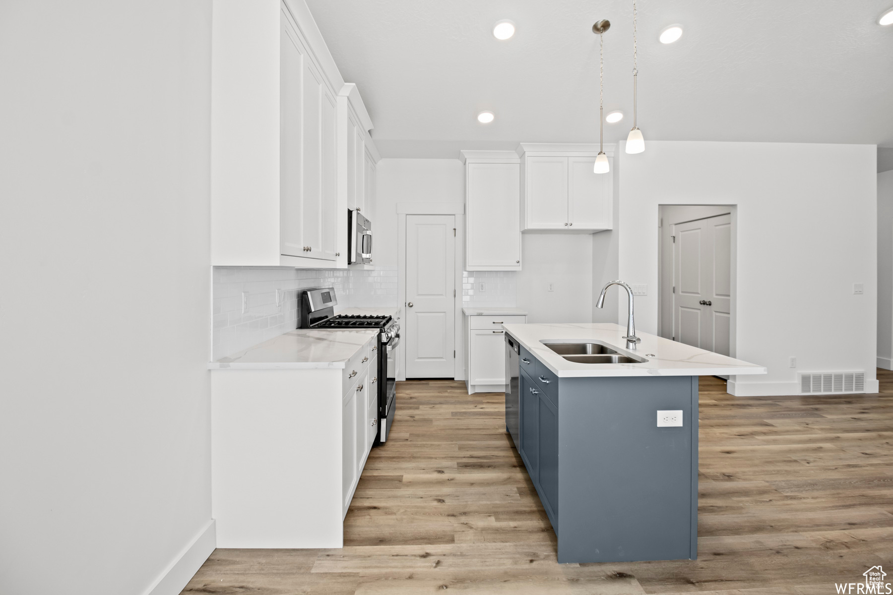 Kitchen with appliances with stainless steel finishes, light hardwood / wood-style flooring, a center island with sink, white cabinets, and sink