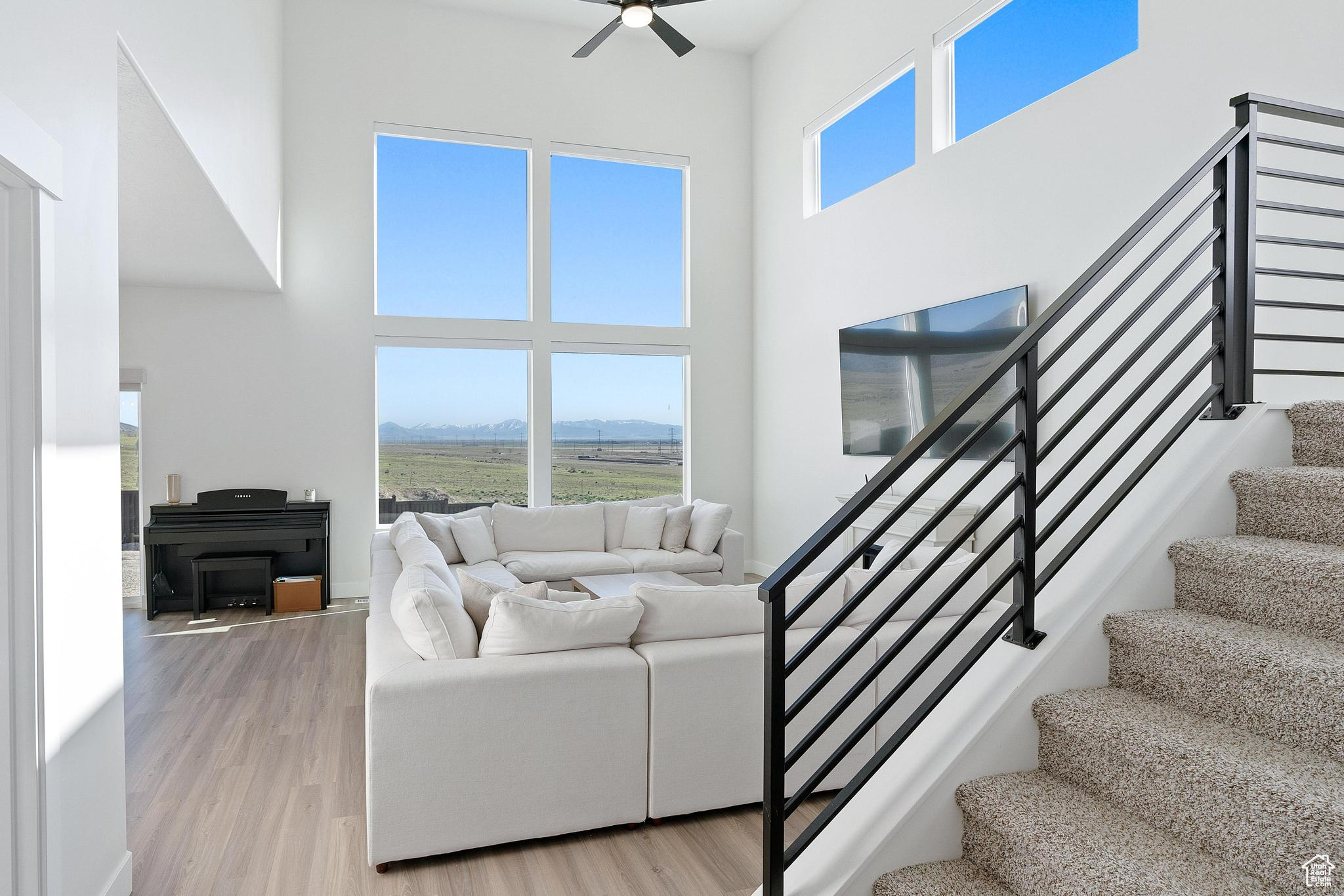 Living room with light hardwood / wood-style flooring, ceiling fan, and a high ceiling