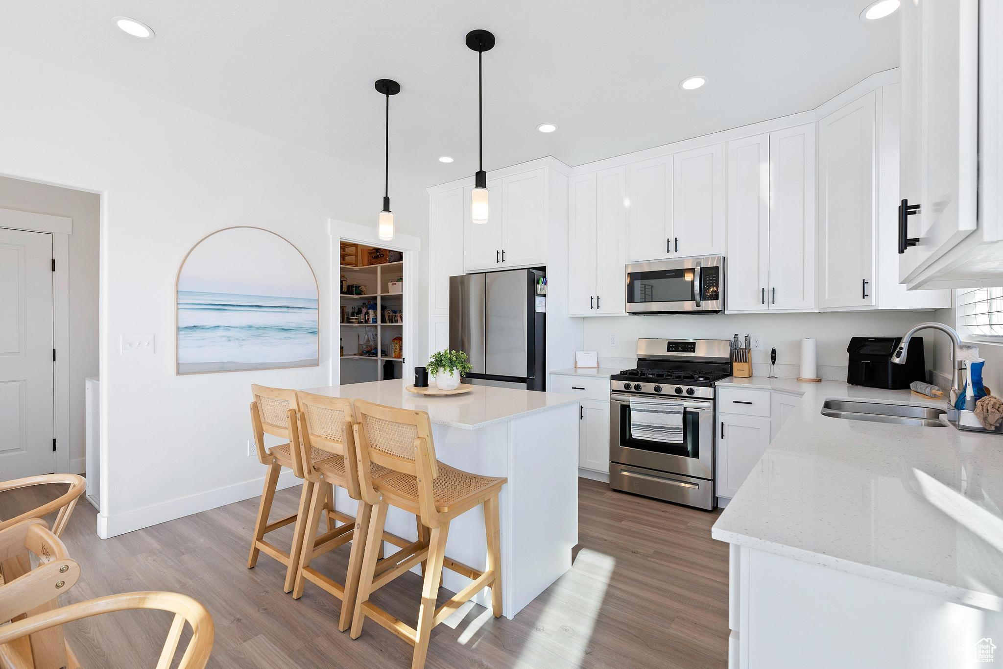 Kitchen with decorative light fixtures, light hardwood / wood-style flooring, stainless steel appliances, sink, and a center island