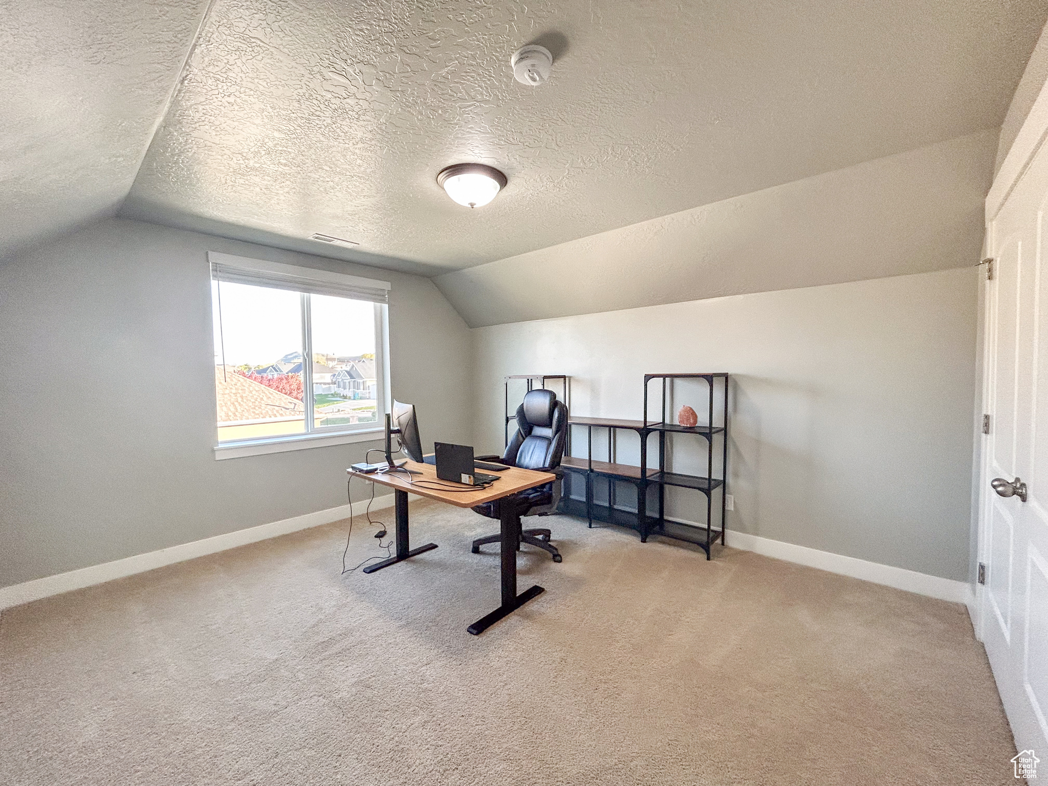 Carpeted office space with vaulted ceiling and a textured ceiling