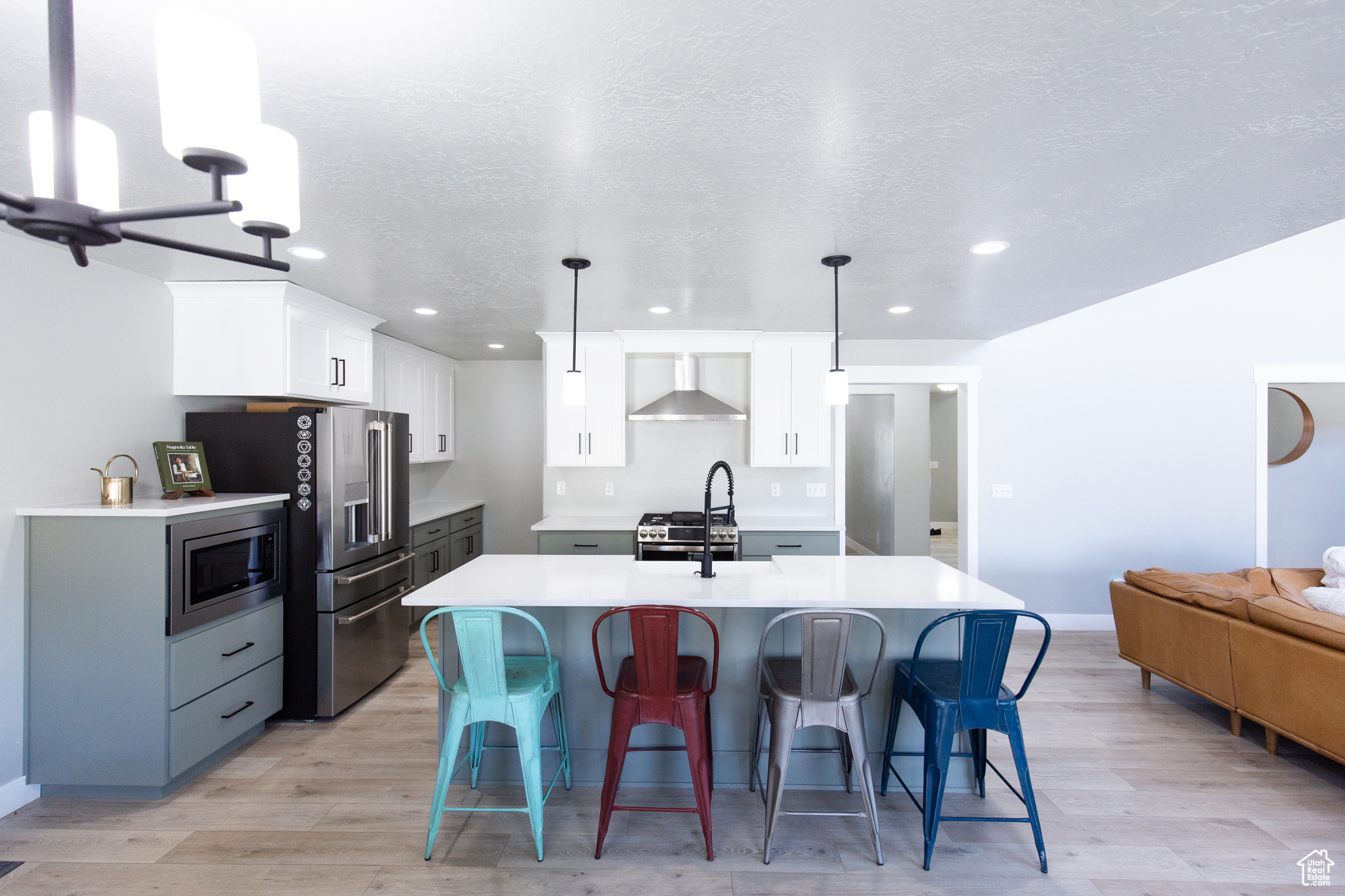 Kitchen featuring appliances with stainless steel finishes, wall chimney range hood, white cabinets, pendant lighting, and light wood-type flooring