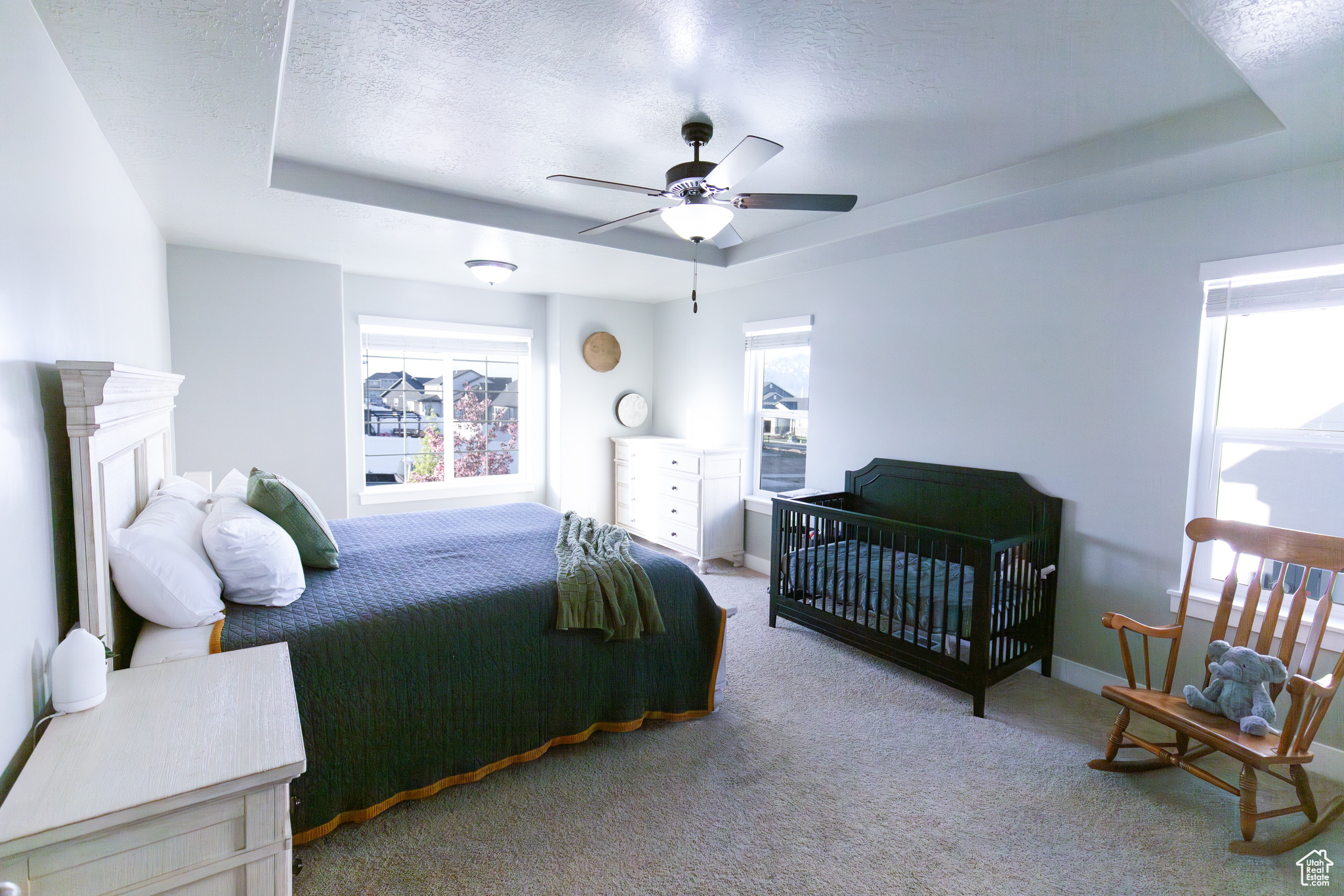 Carpeted bedroom featuring ceiling fan, a tray ceiling, and multiple windows