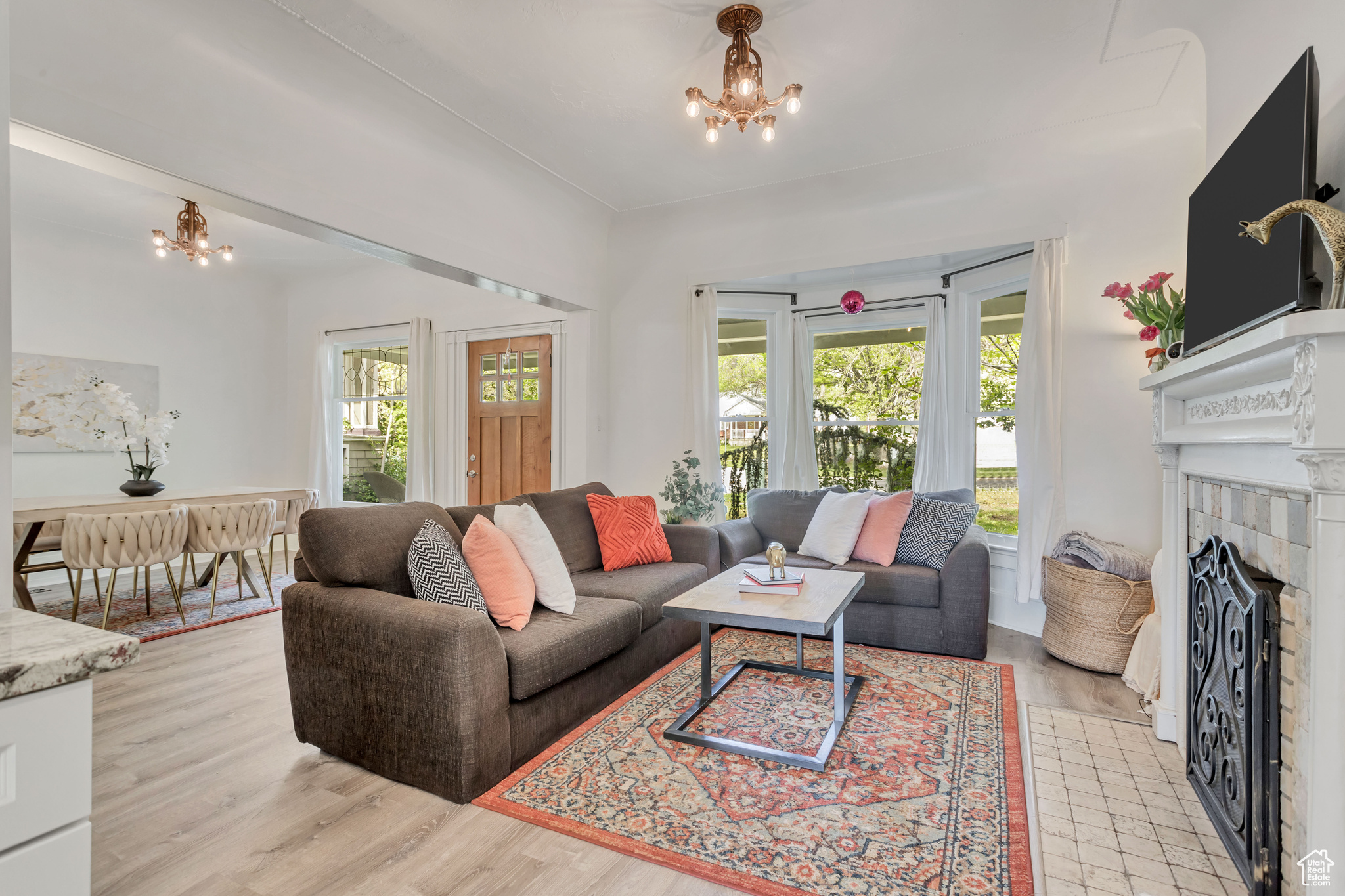 Spacious living room features large bay window for natural light, tiled fireplace with carved mantel and an antique chandelier