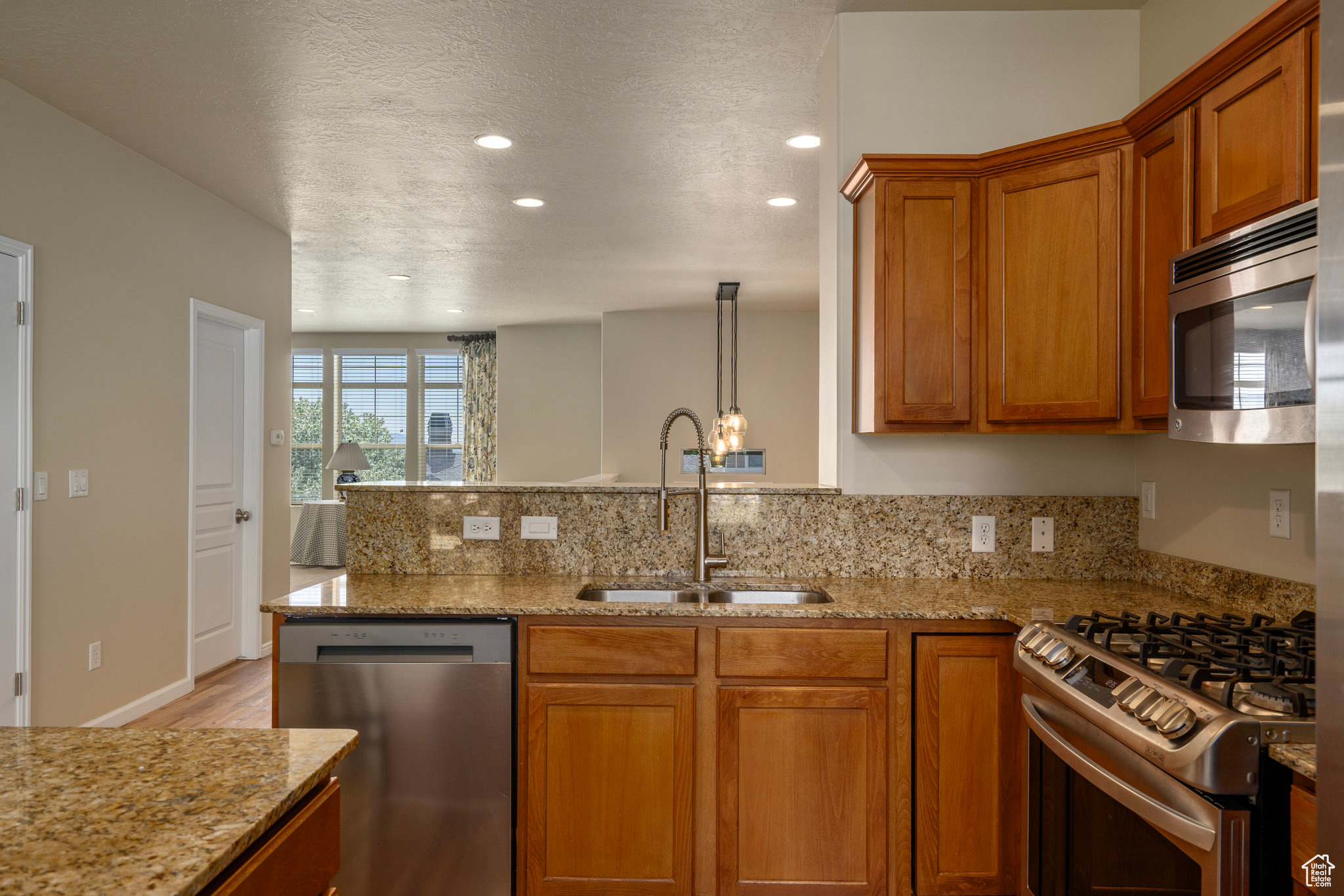 Kitchen with appliances with stainless steel finishes, a textured ceiling, light stone counters, sink, and light wood-type flooring