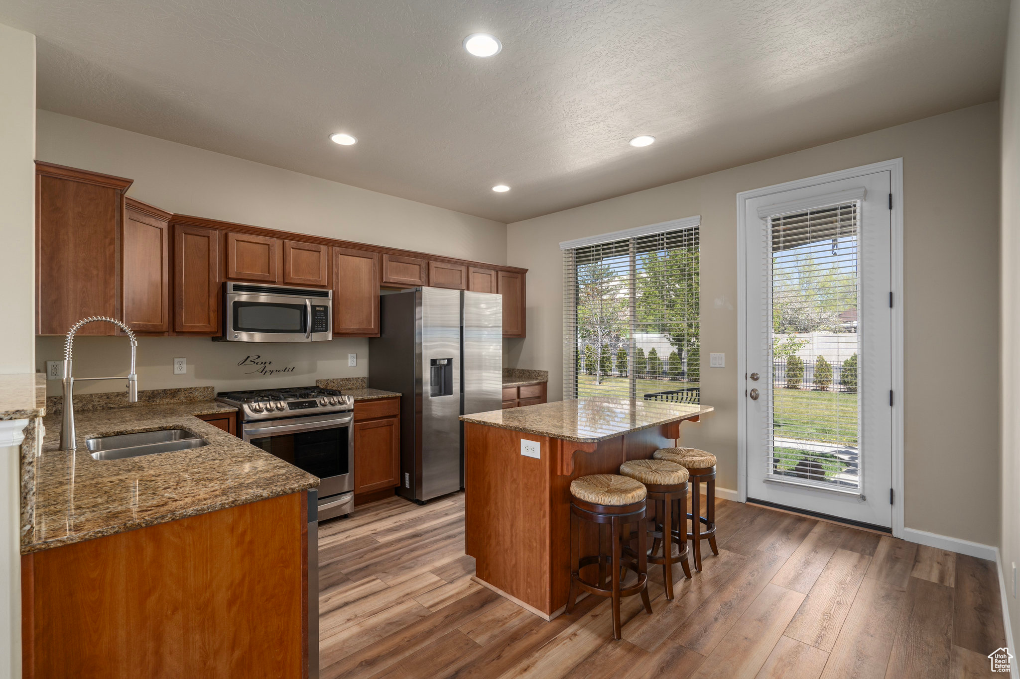 Kitchen with hardwood / wood-style floors, appliances with stainless steel finishes, a center island, and a kitchen breakfast bar