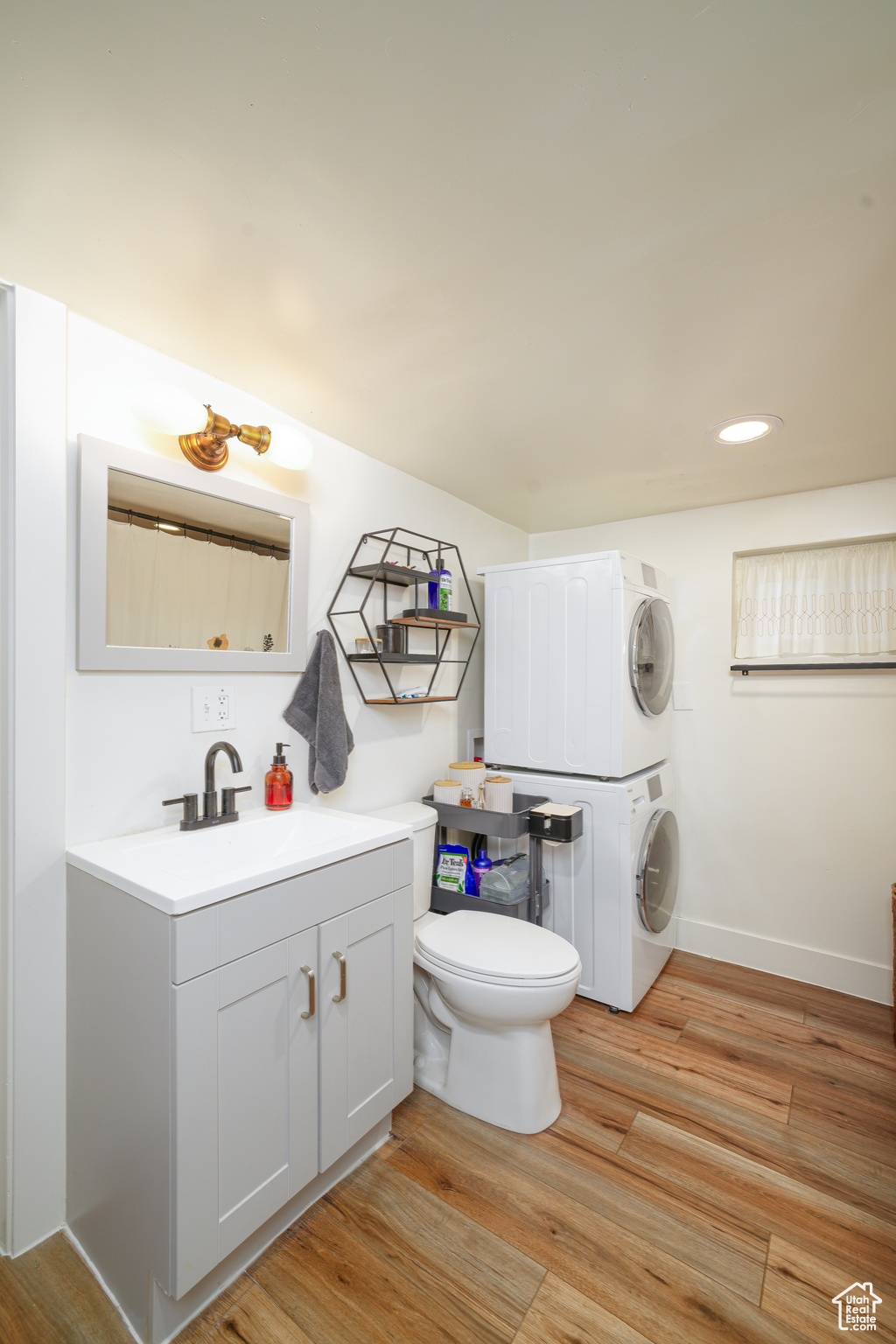 Bathroom featuring laminate flooring, vanity with extensive cabinet space, toilet, and stacked washer and clothes dryer