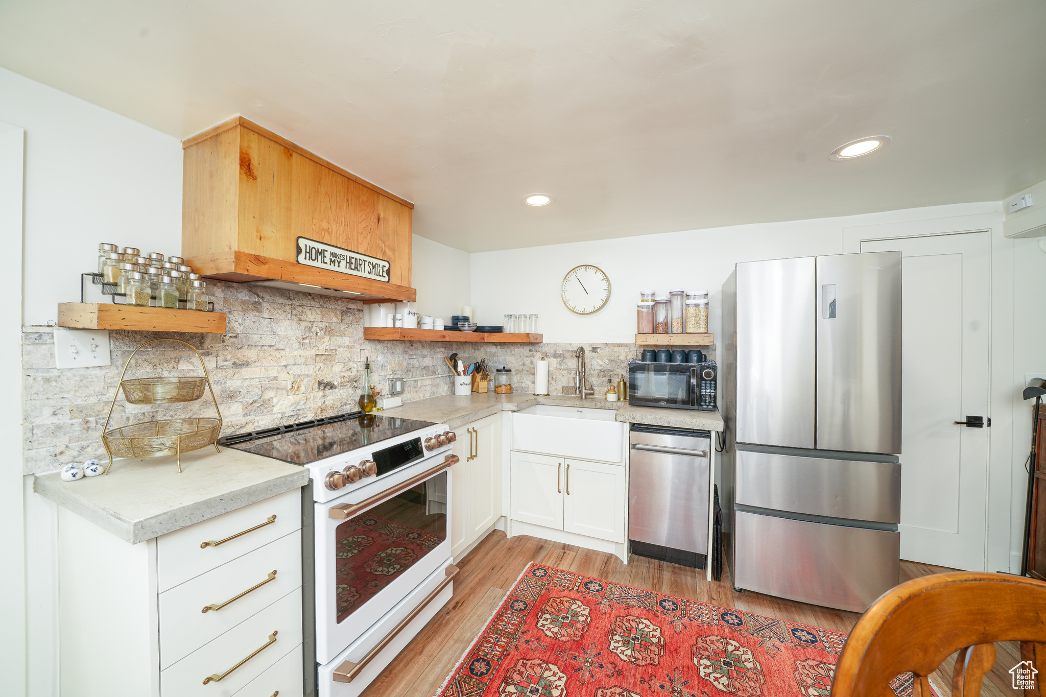Kitchen with light laminate flooring, stainless steel appliances, tasteful backsplash, white cabinets, and sink