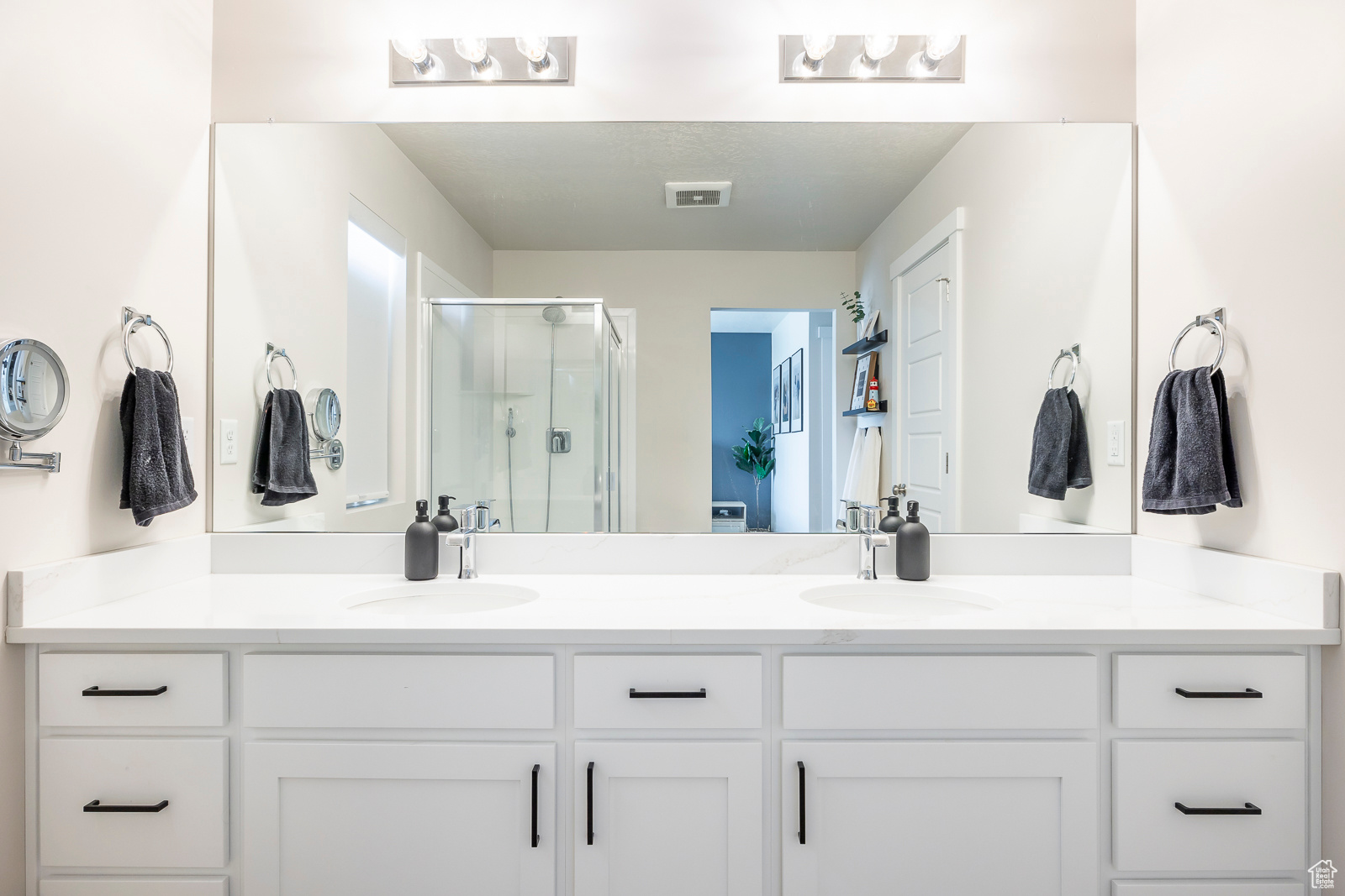 Bathroom with vanity with extensive cabinet space, dual sinks, and a shower with shower door