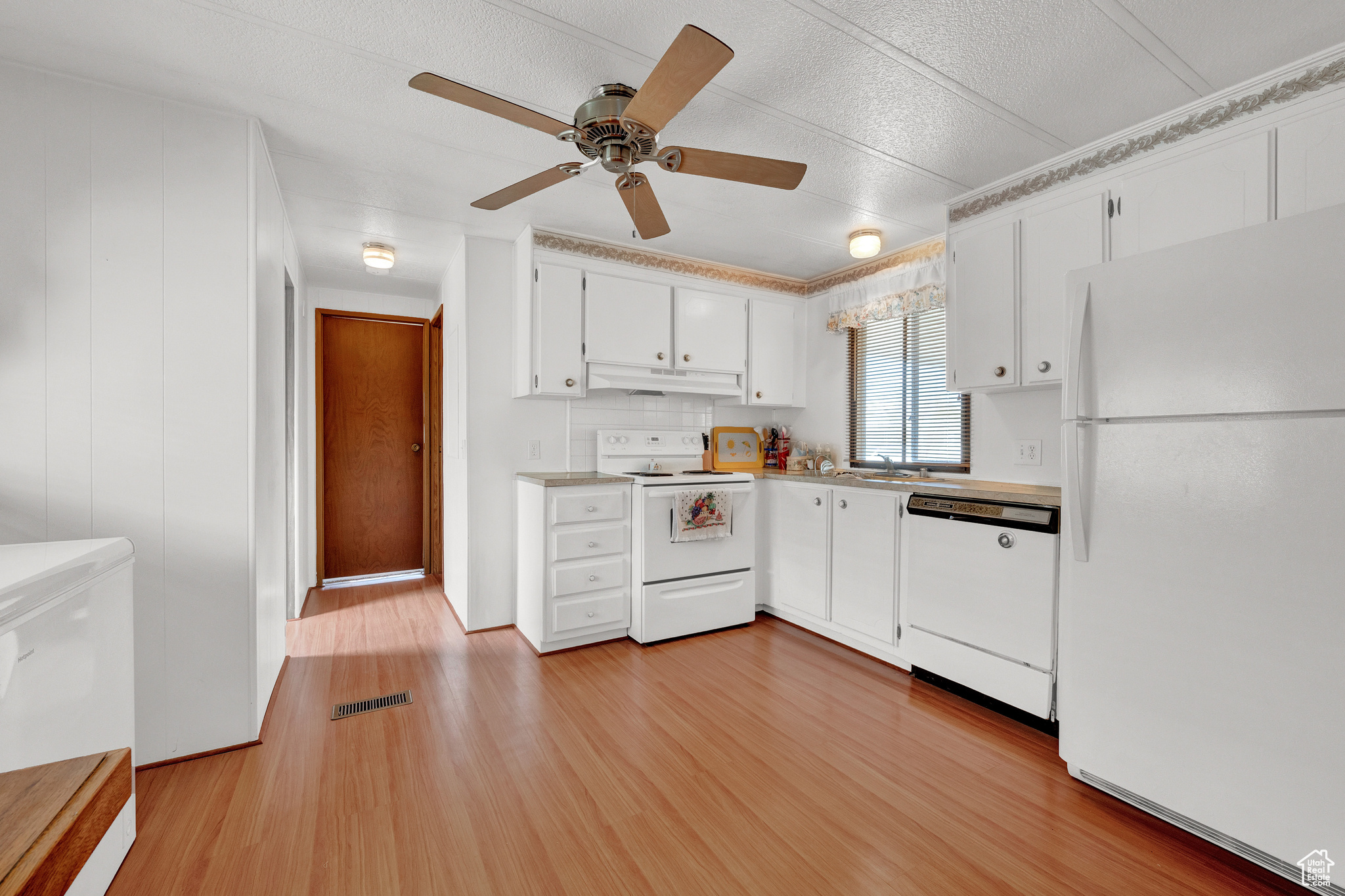 Kitchen featuring white appliances, light wood-type flooring, white cabinetry, ceiling fan, and a textured ceiling
