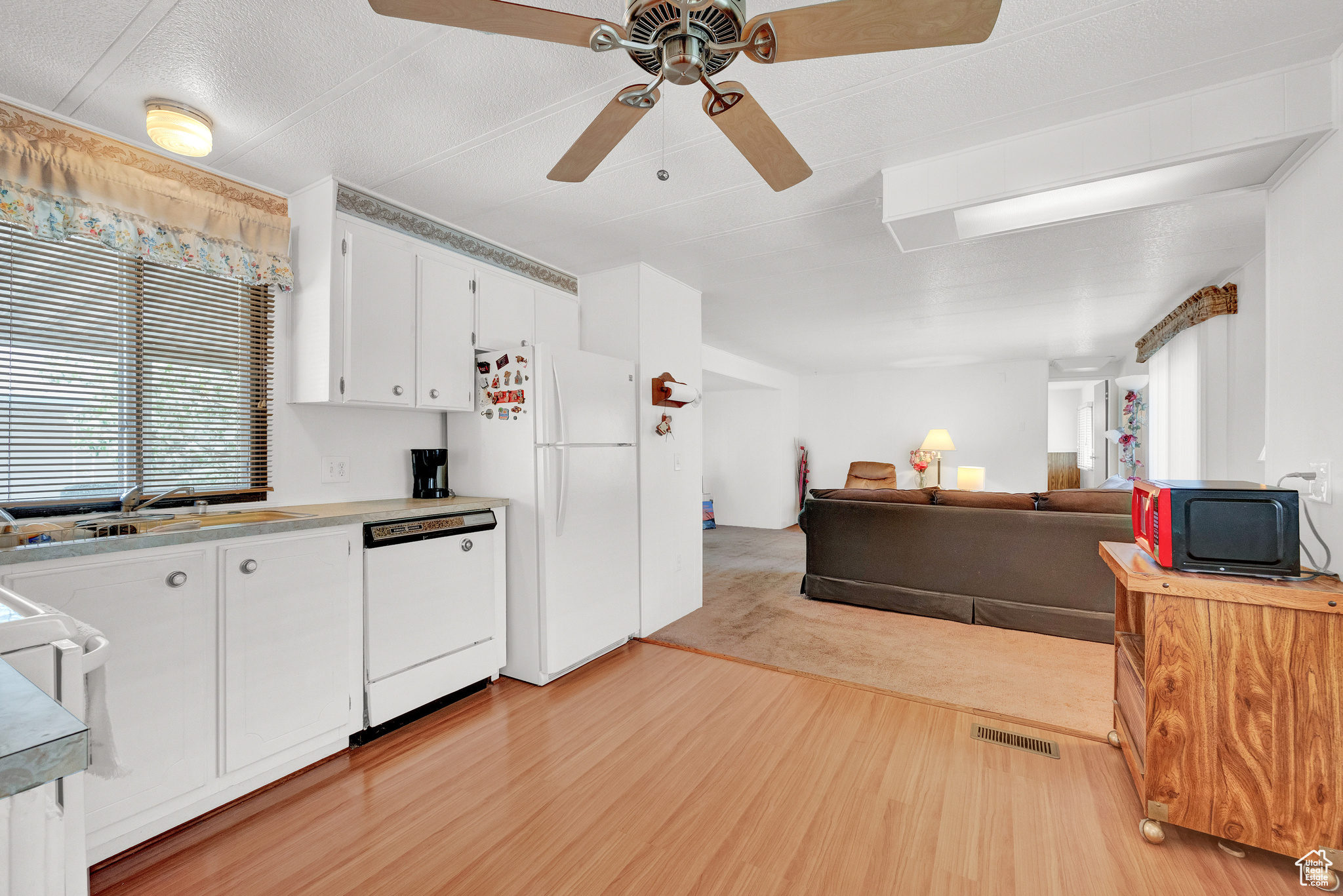 Kitchen featuring ceiling fan, sink, white appliances, white cabinetry, and light colored carpet