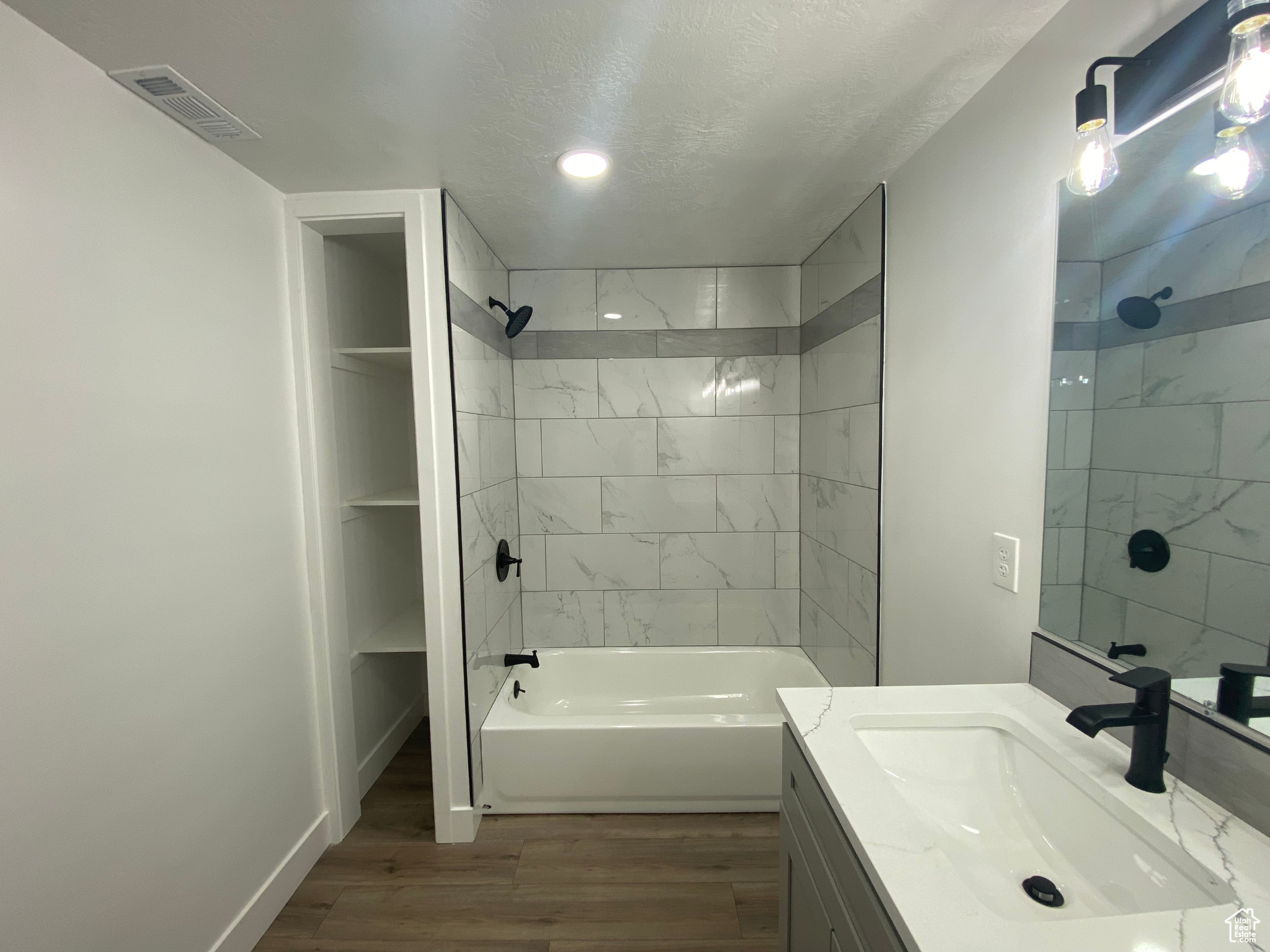 Bathroom featuring wood-type flooring, tiled shower / bath combo, large vanity, and a textured ceiling