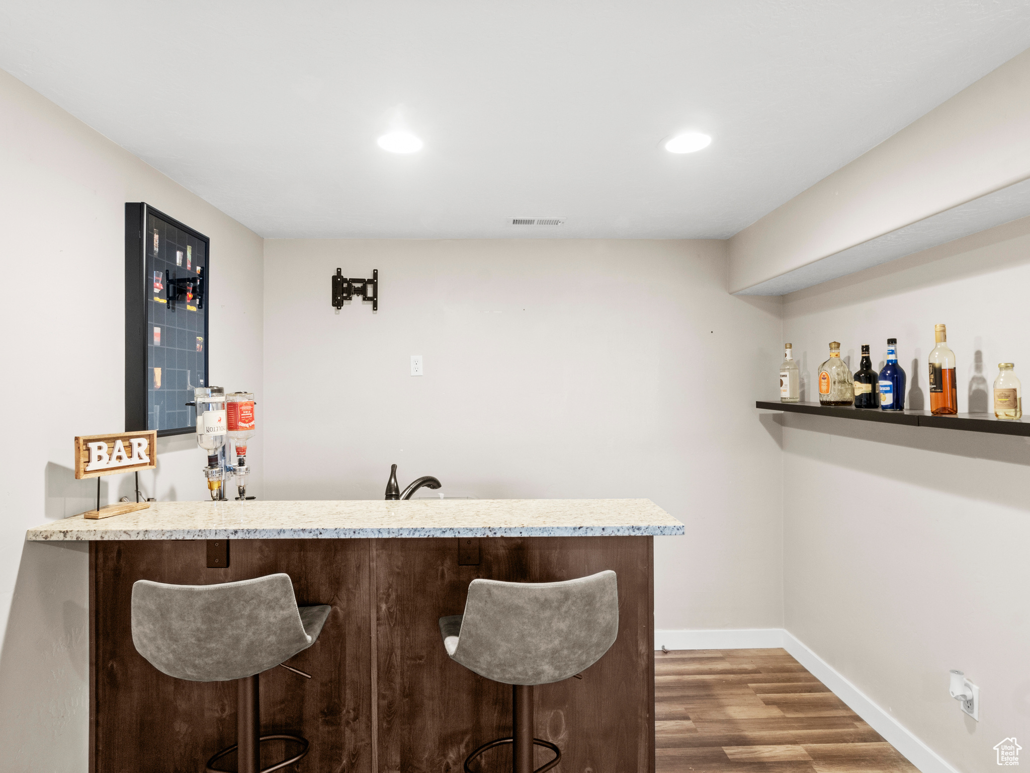 Bar with light stone countertops and hardwood / wood-style flooring