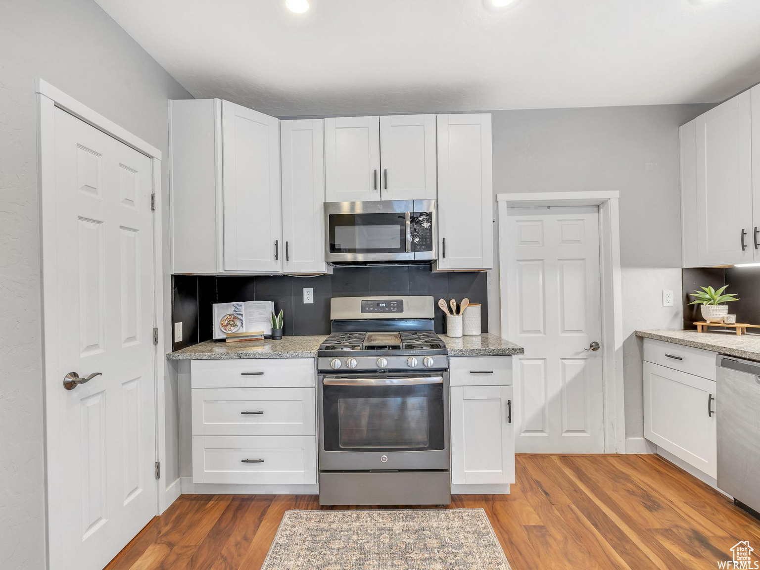 Updated Kitchen with light stone countertops, appliances with stainless steel finishes, light hardwood / wood-style flooring, backsplash, and white cabinets