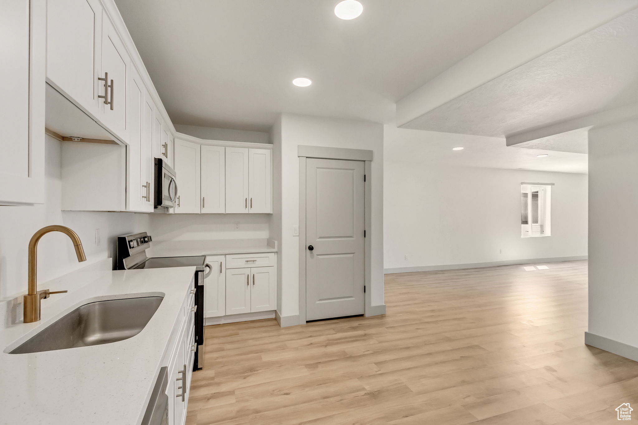 Kitchen with sink, light hardwood / wood-style flooring, white cabinetry, and appliances with stainless steel finishes