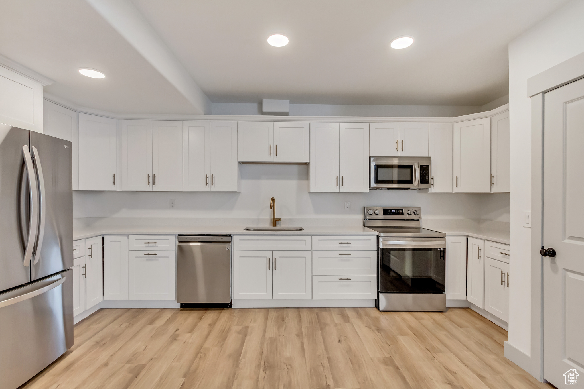 Kitchen featuring white cabinets, sink, appliances with stainless steel finishes, and light wood-type flooring