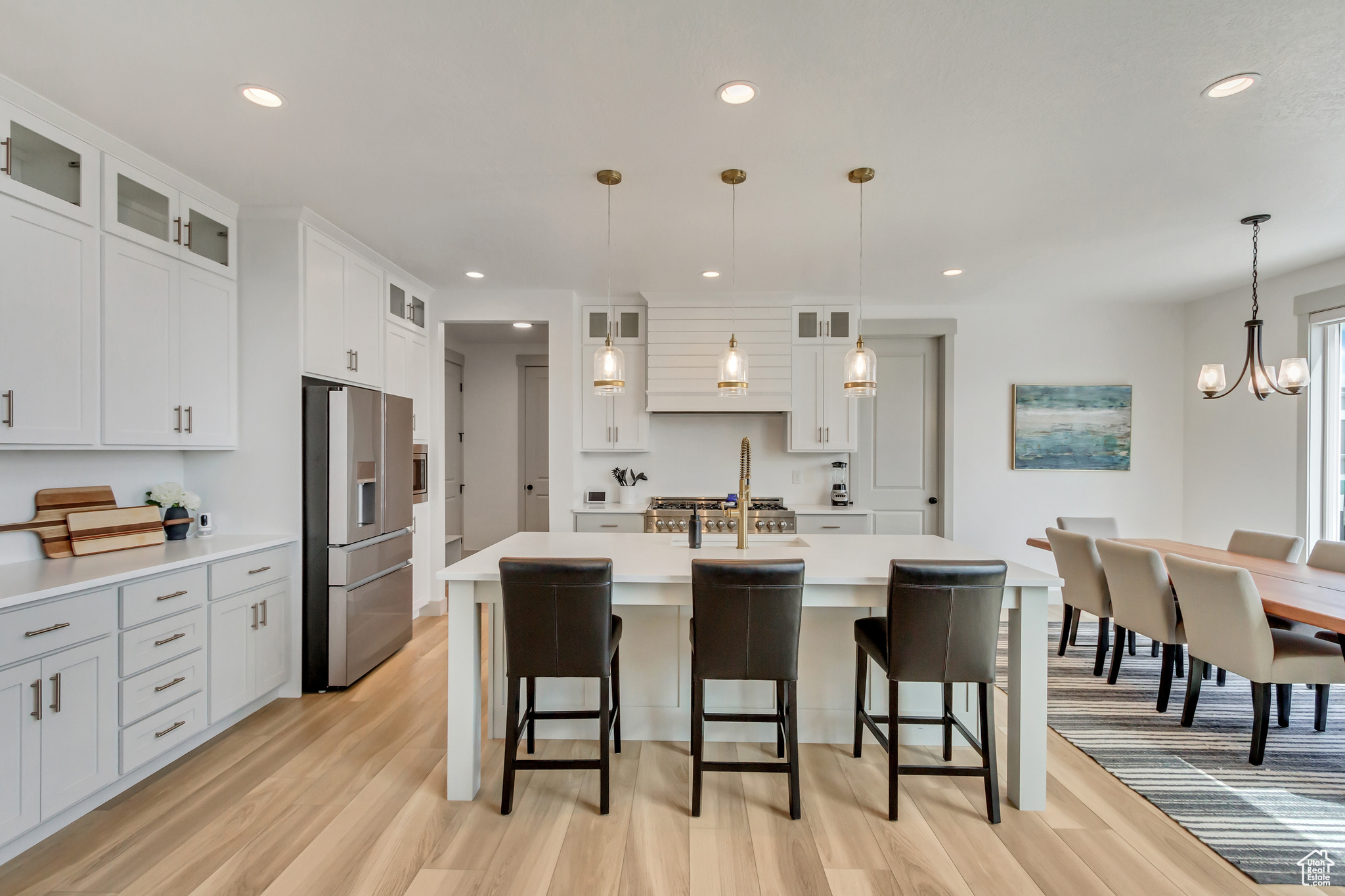 Kitchen featuring stainless steel fridge with ice dispenser, decorative light fixtures, a center island with sink, light hardwood / wood-style floors, and white cabinetry