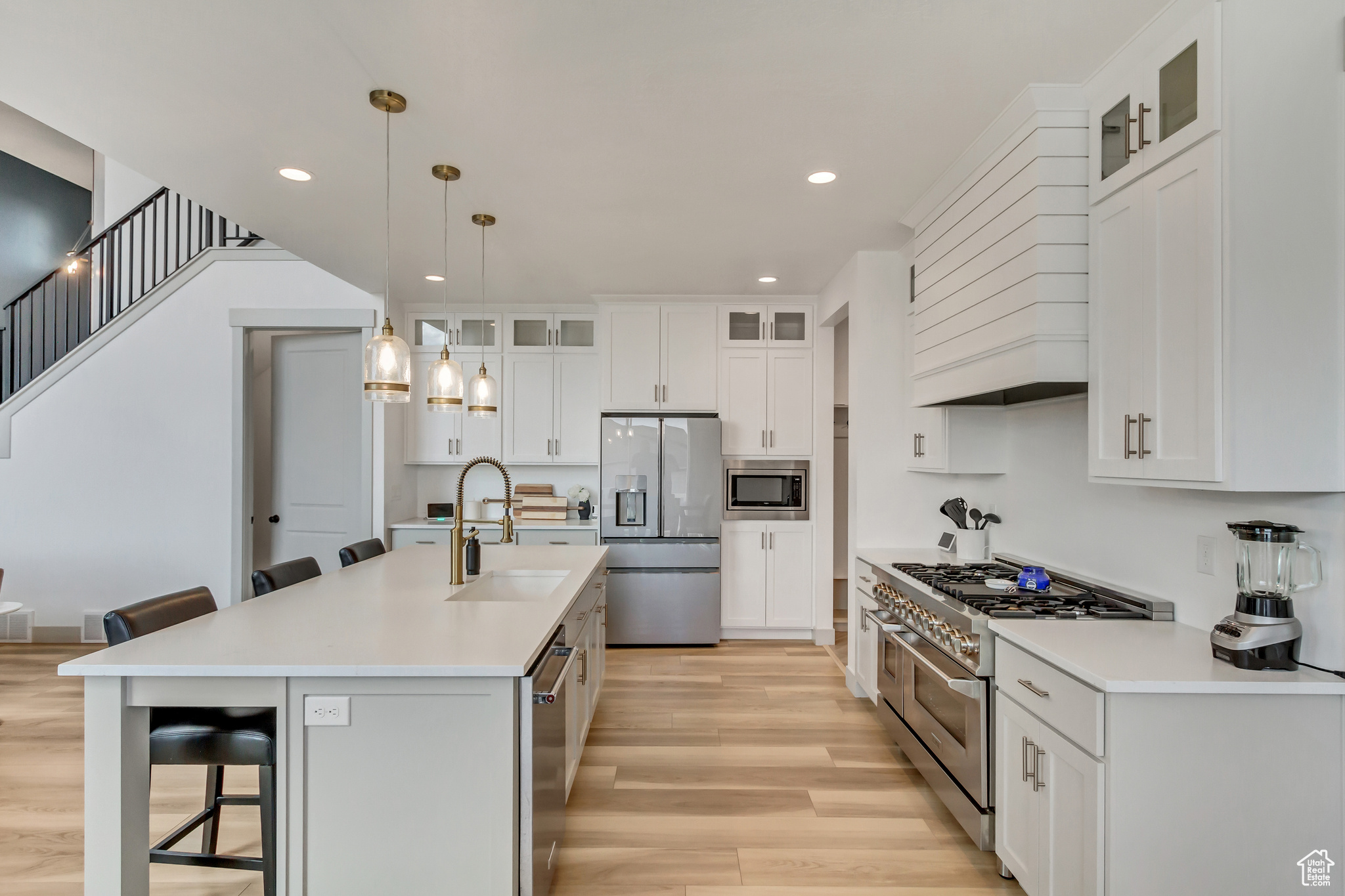 Kitchen featuring sink, light wood-type flooring, stainless steel appliances, premium range hood, and pendant lighting
