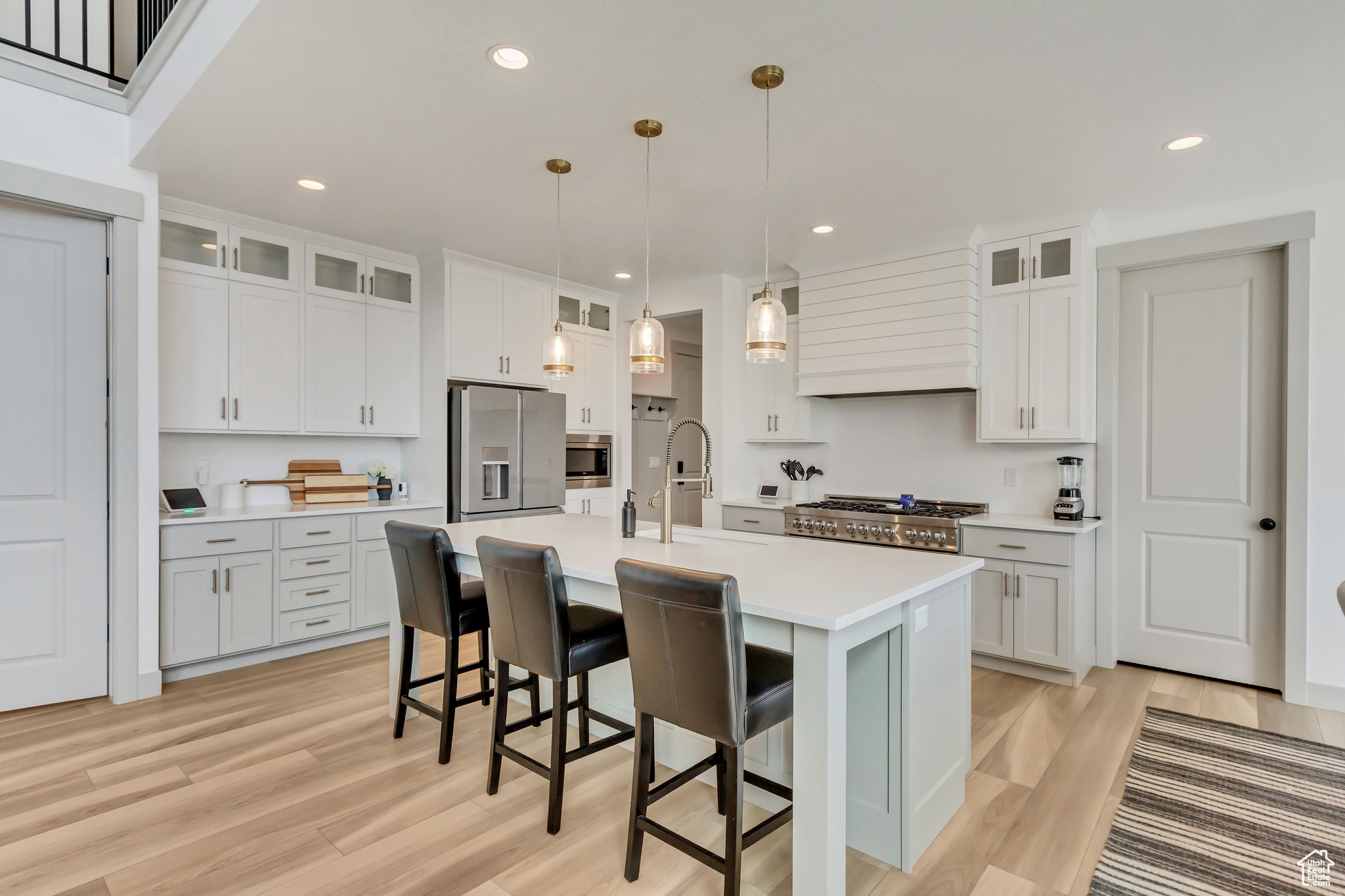 Kitchen with appliances with stainless steel finishes, light hardwood / wood-style flooring, a center island with sink, white cabinets, and sink