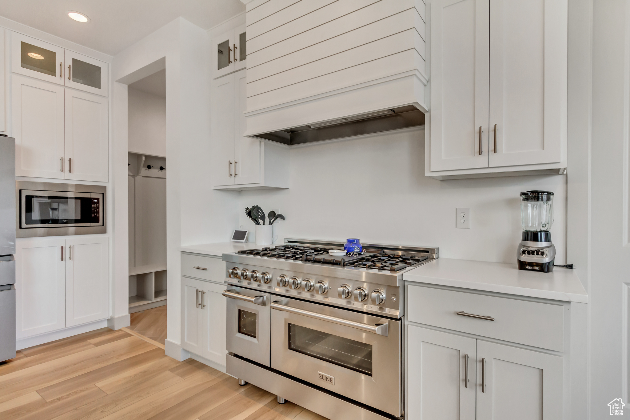 Kitchen featuring white cabinets, appliances with stainless steel finishes, custom range hood, and light hardwood / wood-style flooring