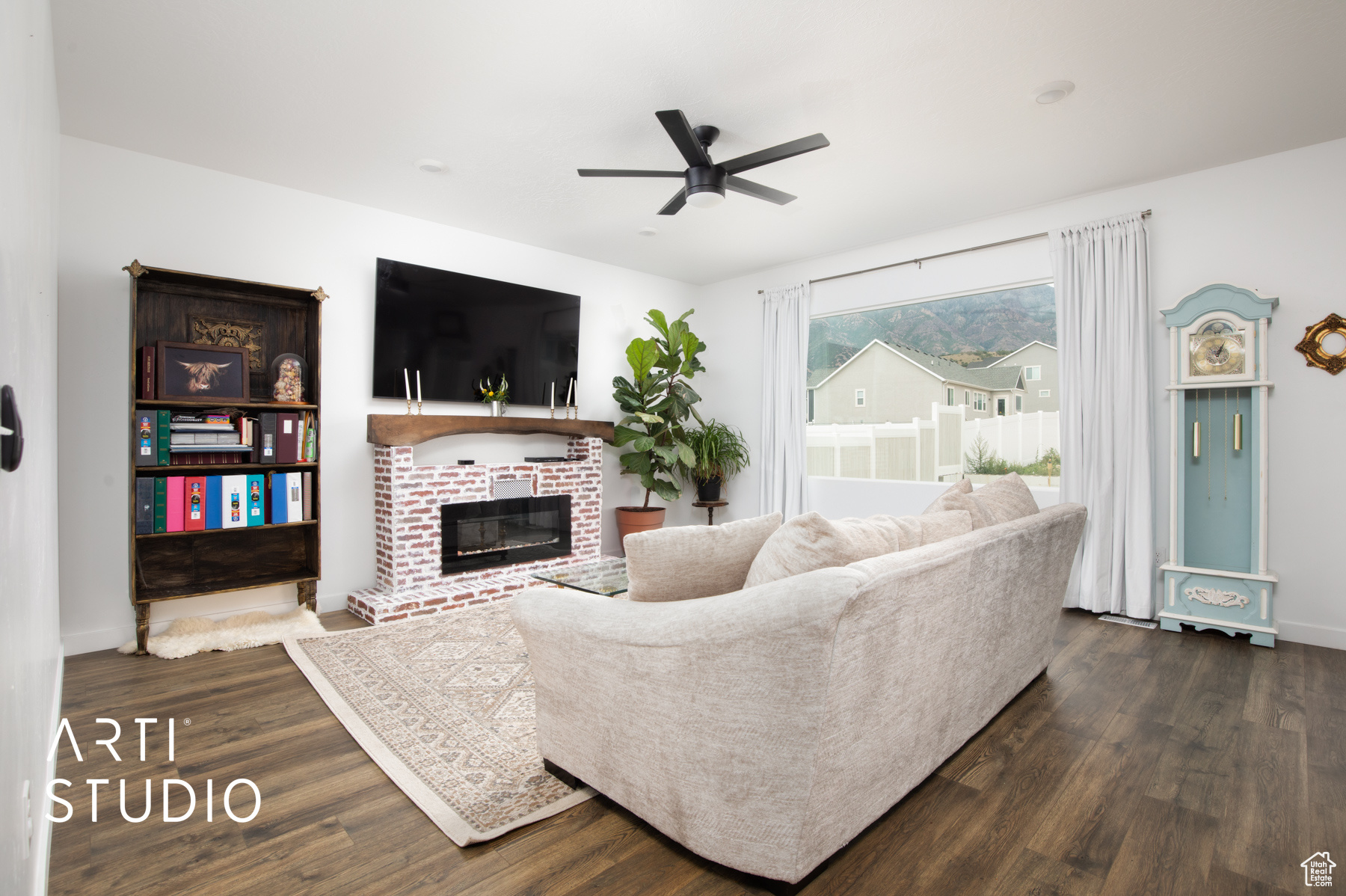 Living room featuring ceiling fan, dark wood-type flooring, and a brick fireplace