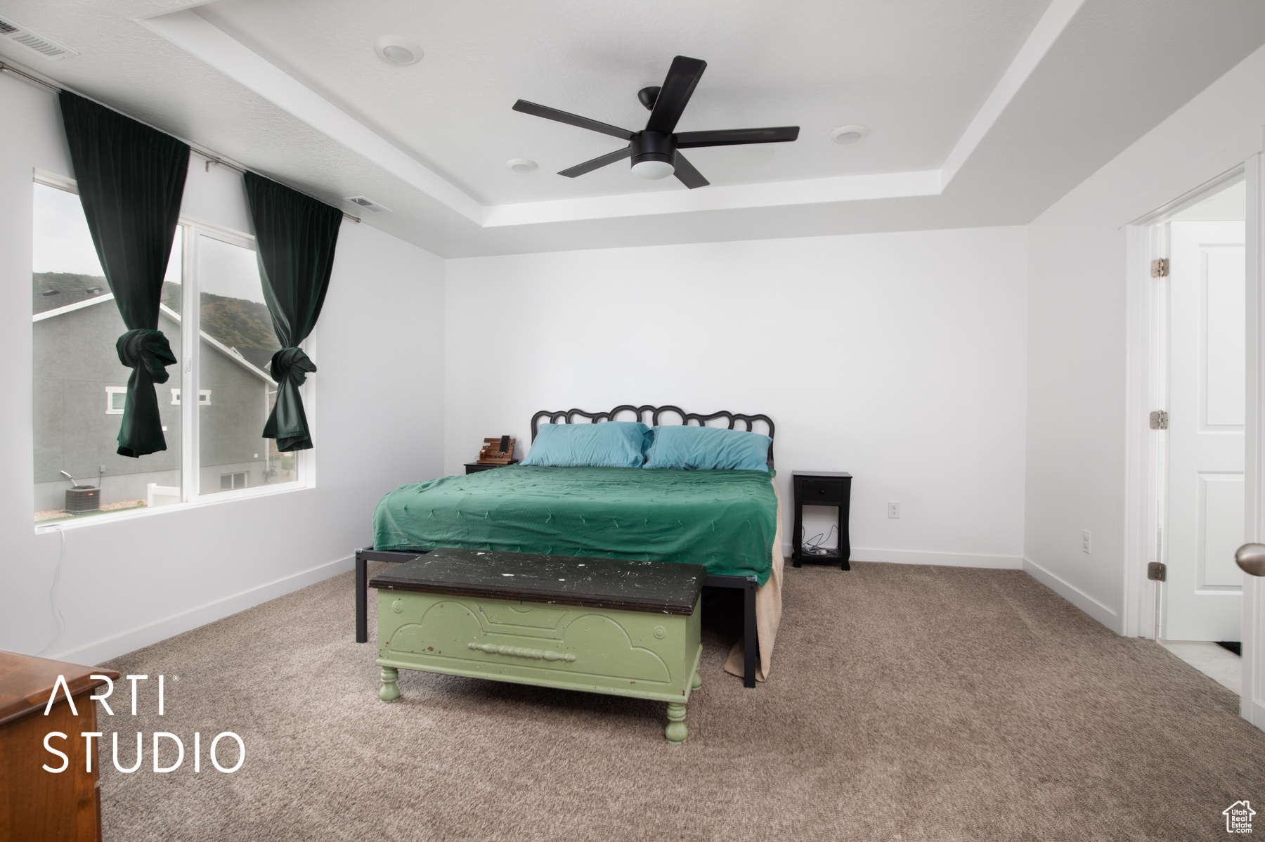 Carpeted bedroom featuring ceiling fan and a raised ceiling