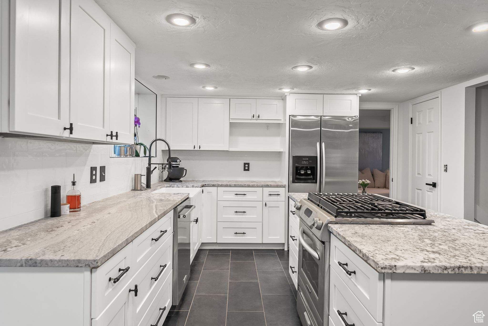 Kitchen featuring light stone countertops, white cabinetry, appliances with stainless steel finishes, tasteful backsplash, and dark tile flooring
