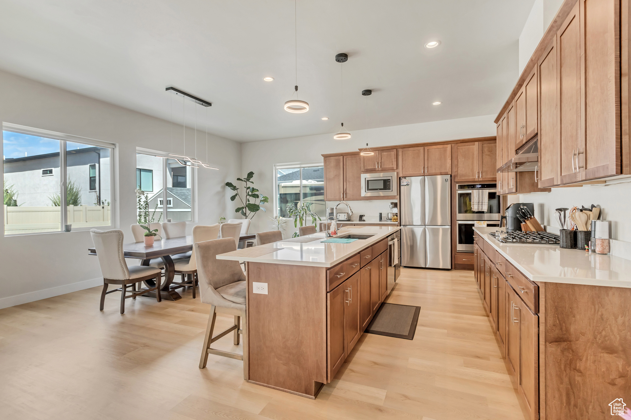 Kitchen with a kitchen bar, appliances with stainless steel finishes, light hardwood / wood-style flooring, a center island with sink, and pendant lighting