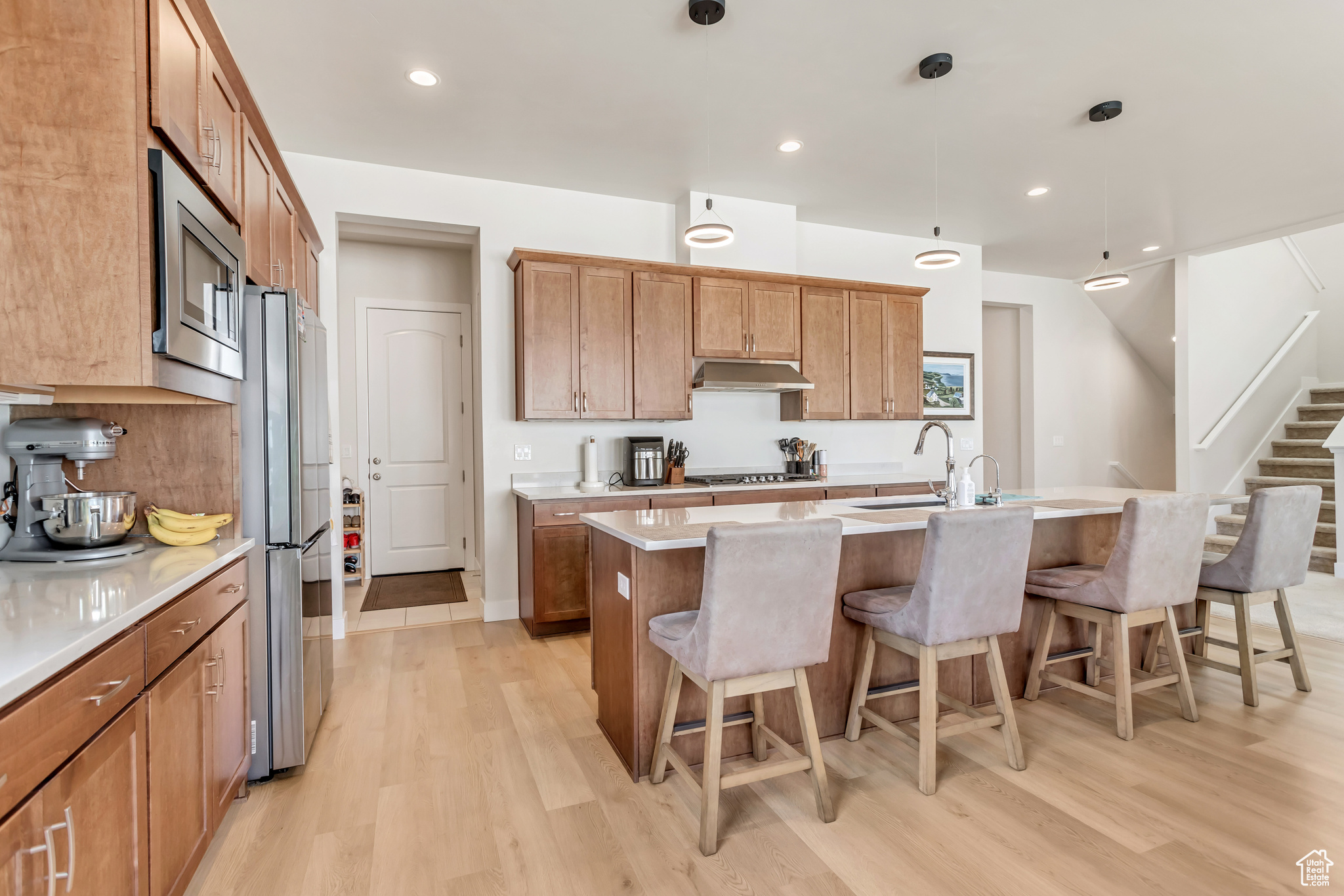 Kitchen with appliances with stainless steel finishes, light hardwood / wood-style floors, an island with sink, a kitchen breakfast bar, and sink