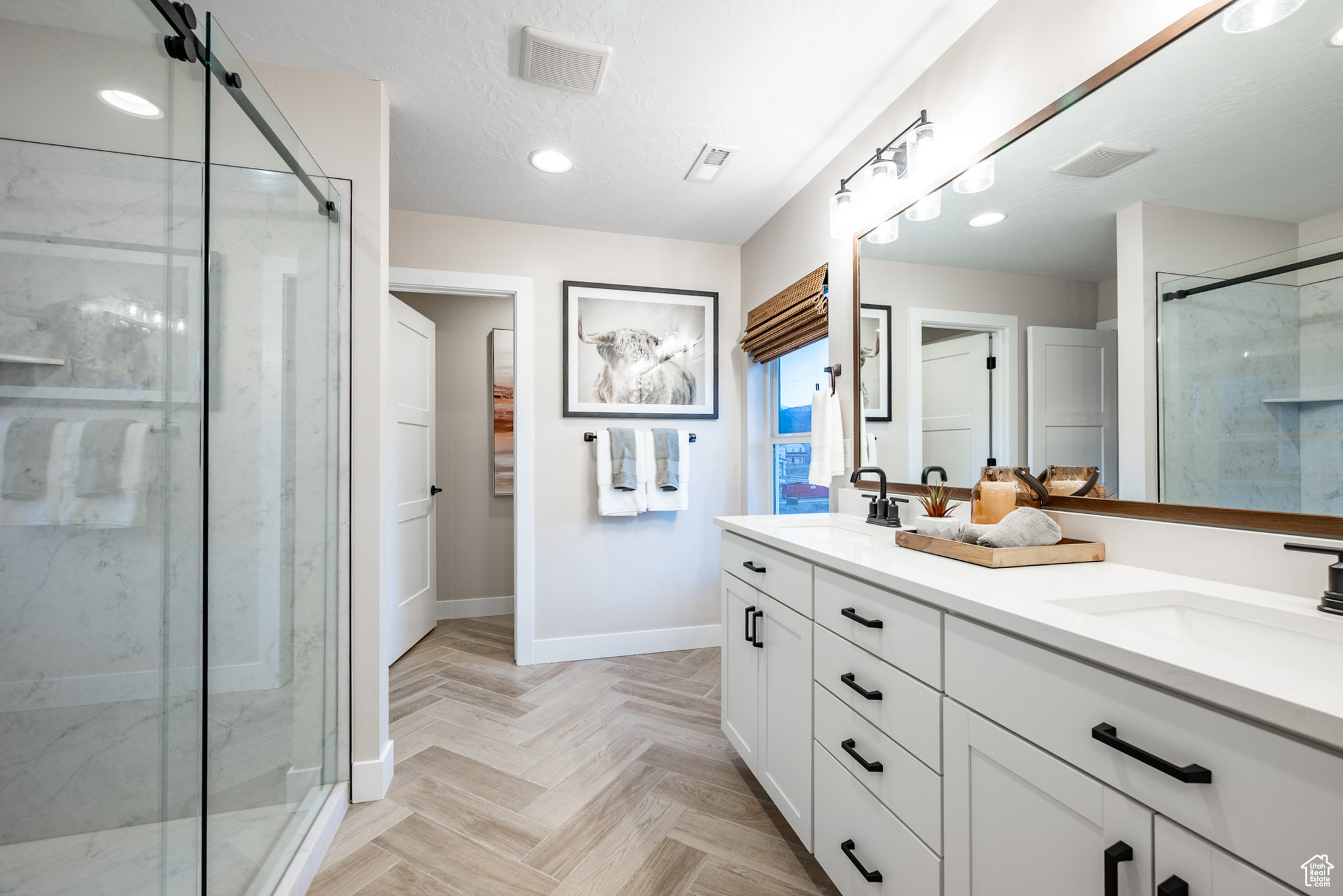 Bathroom featuring dual sinks, large vanity, an enclosed shower, and parquet flooring