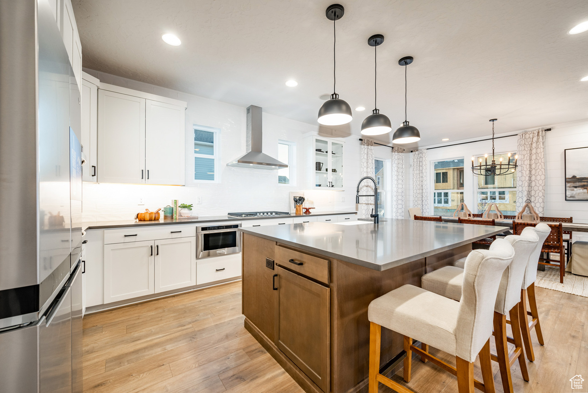 Kitchen featuring decorative light fixtures, appliances with stainless steel finishes, wall chimney exhaust hood, and light hardwood / wood-style flooring
