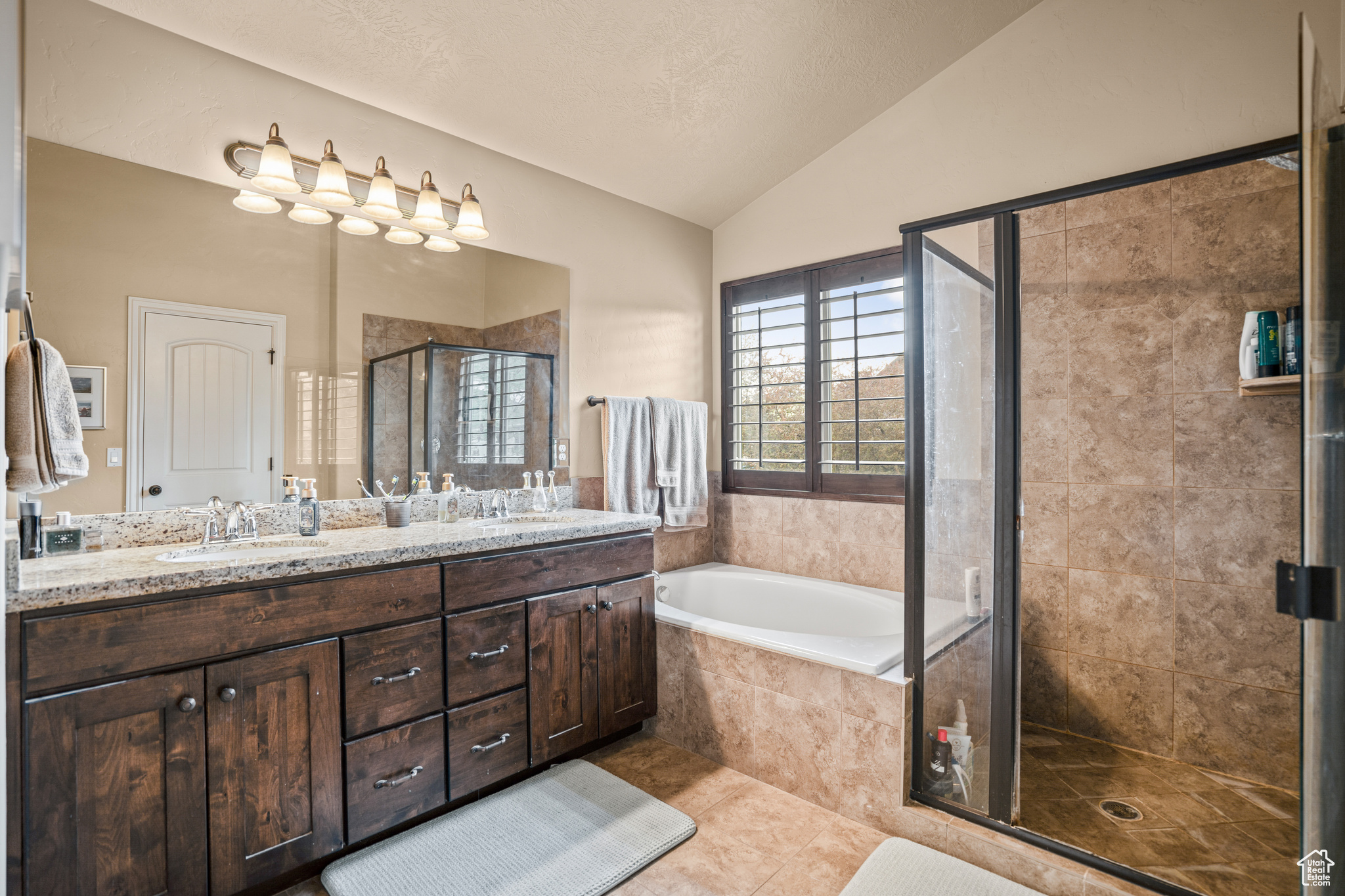 Bathroom featuring oversized vanity, tile flooring, vaulted ceiling, dual sinks, and plus walk in shower