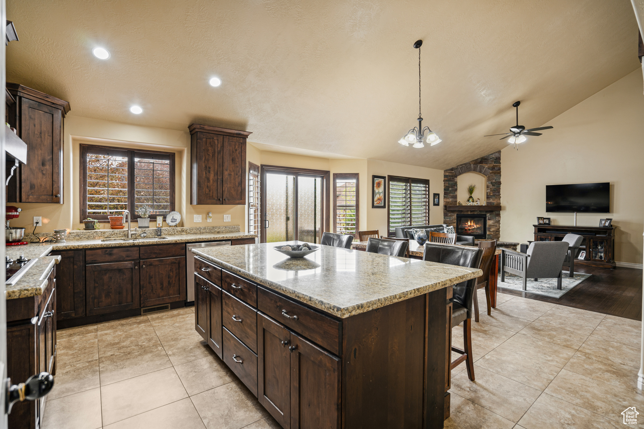 Kitchen featuring light stone counters, a center island, light tile floors, a fireplace, and ceiling fan with notable chandelier