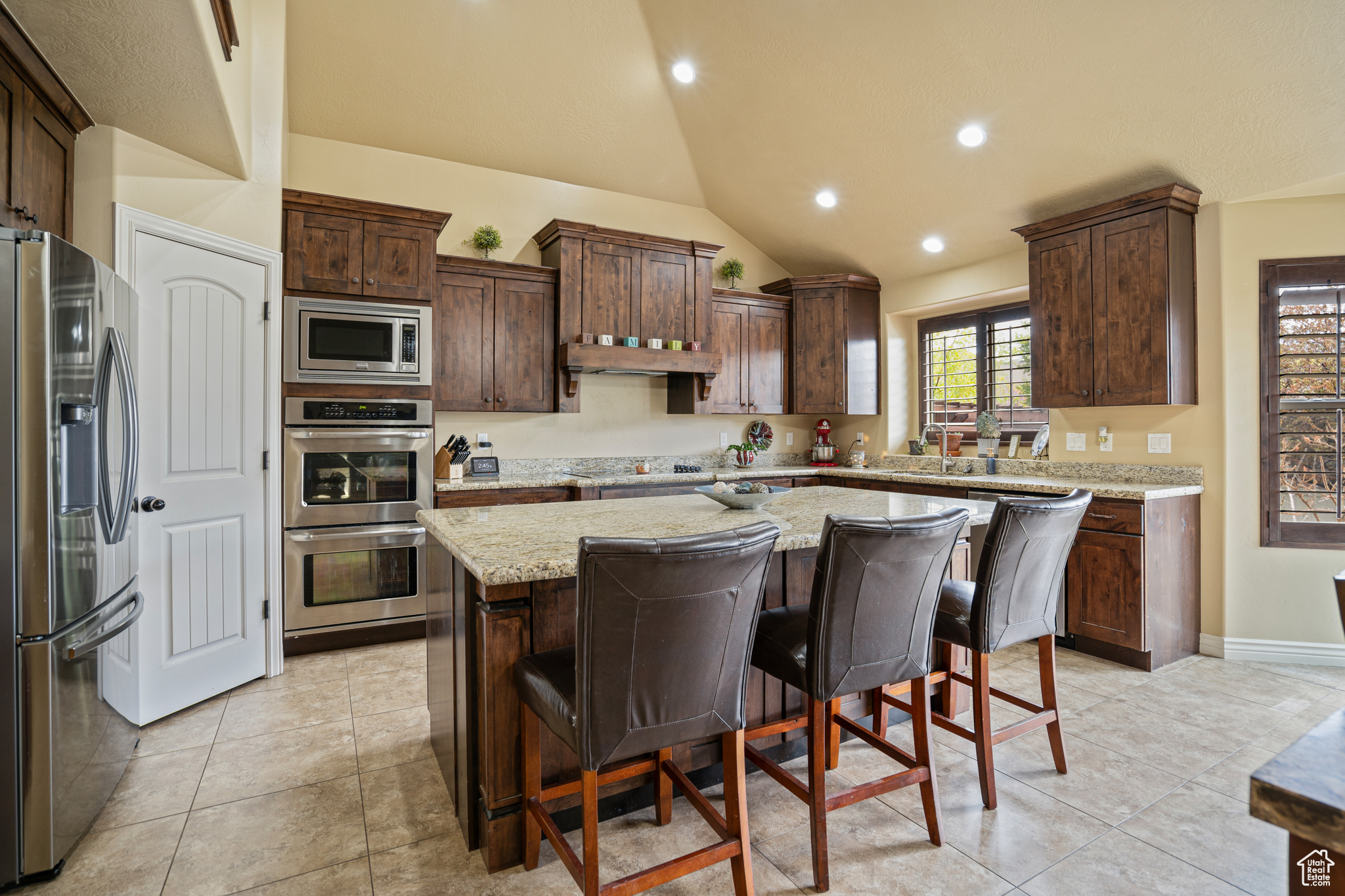 Kitchen featuring light stone counters, a center island, light tile floors, a kitchen bar, and stainless steel appliances