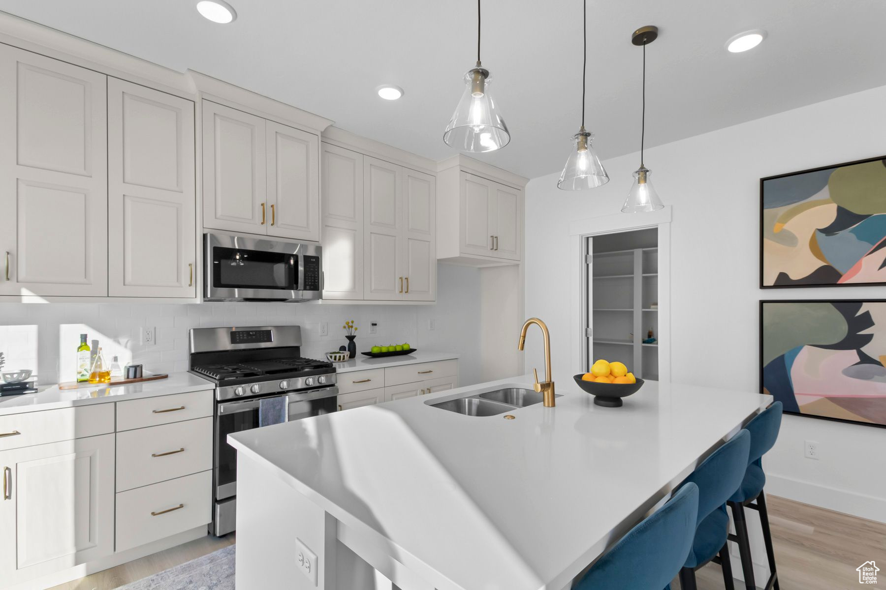 Kitchen featuring appliances with stainless steel finishes, a center island with sink, light hardwood / wood-style floors, tasteful backsplash, and sink